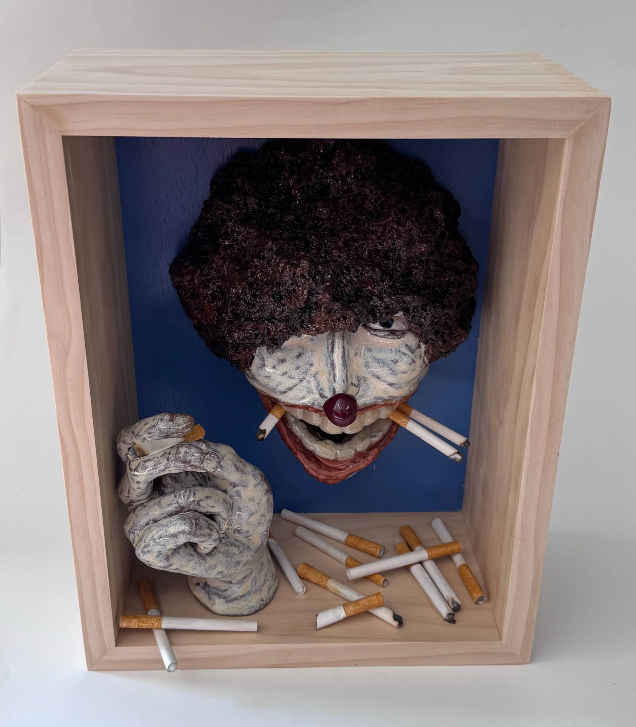 Ariel Choi - Chain smoking Clown, ceramic and paper on wood, 14”x11”x5.5”, 2025