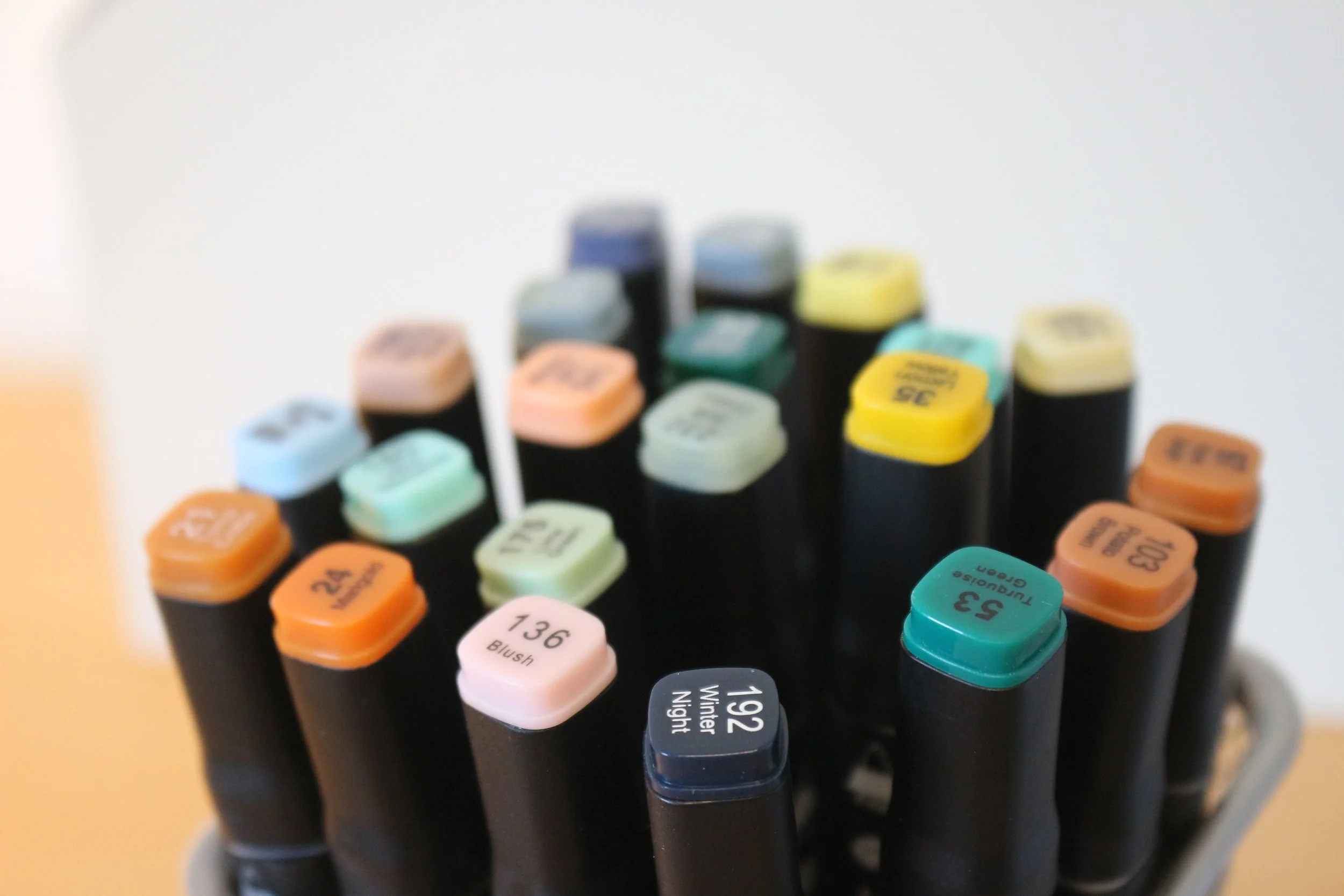 Mehrere Filzstifte in verschiedenen Farben, die Spitze nach oben gerichtet. Die Filzstiftkappen sind in verschiedenen Farben und mit unterschiedlich beschrifteten Labels versehen.