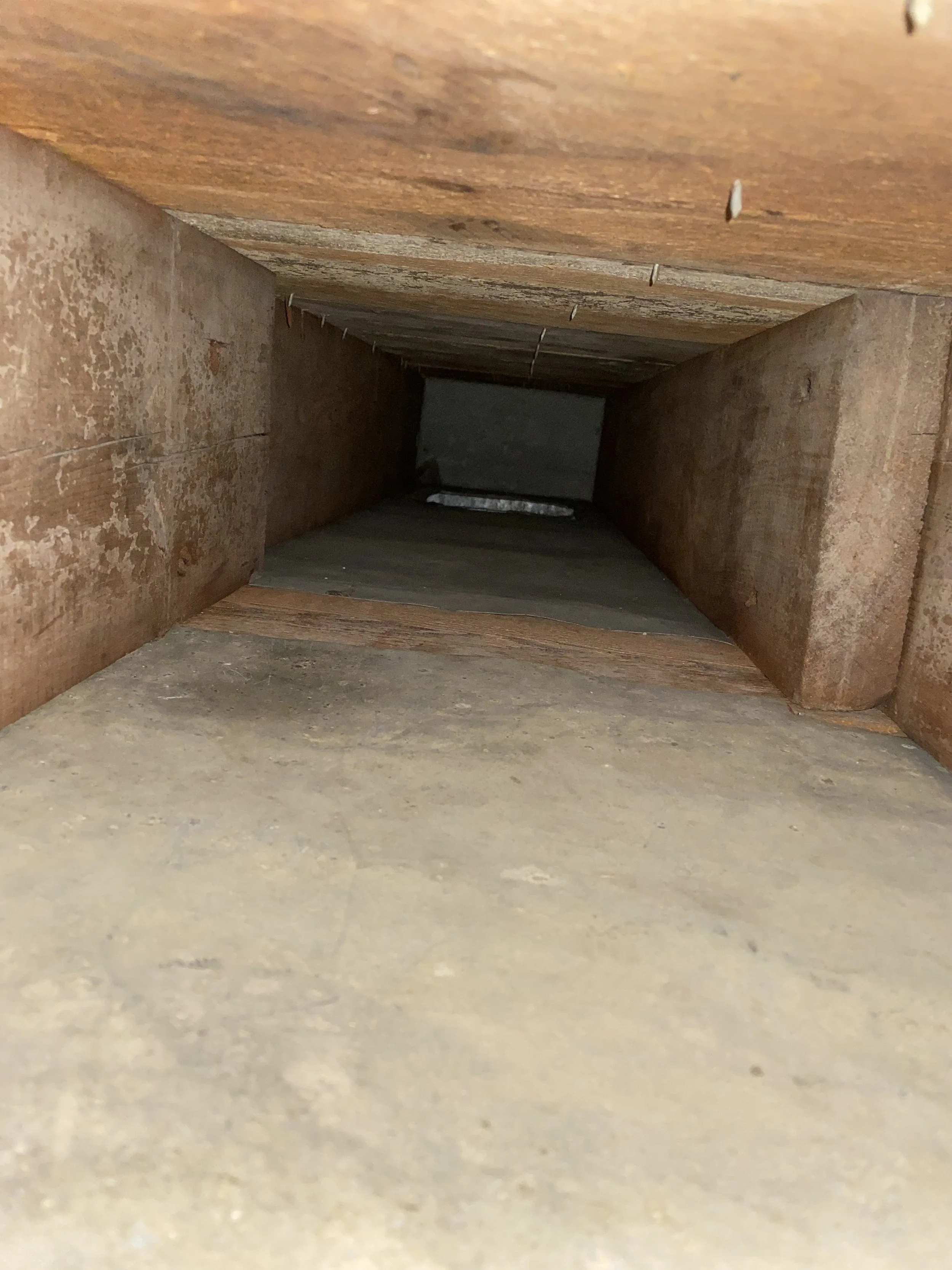 Looking inside a wooden chimney or vent shaft from below, showing the interior with wood and concrete surfaces.