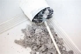 Clogged drainpipe with gray debris spilling onto white floor with baseboard.