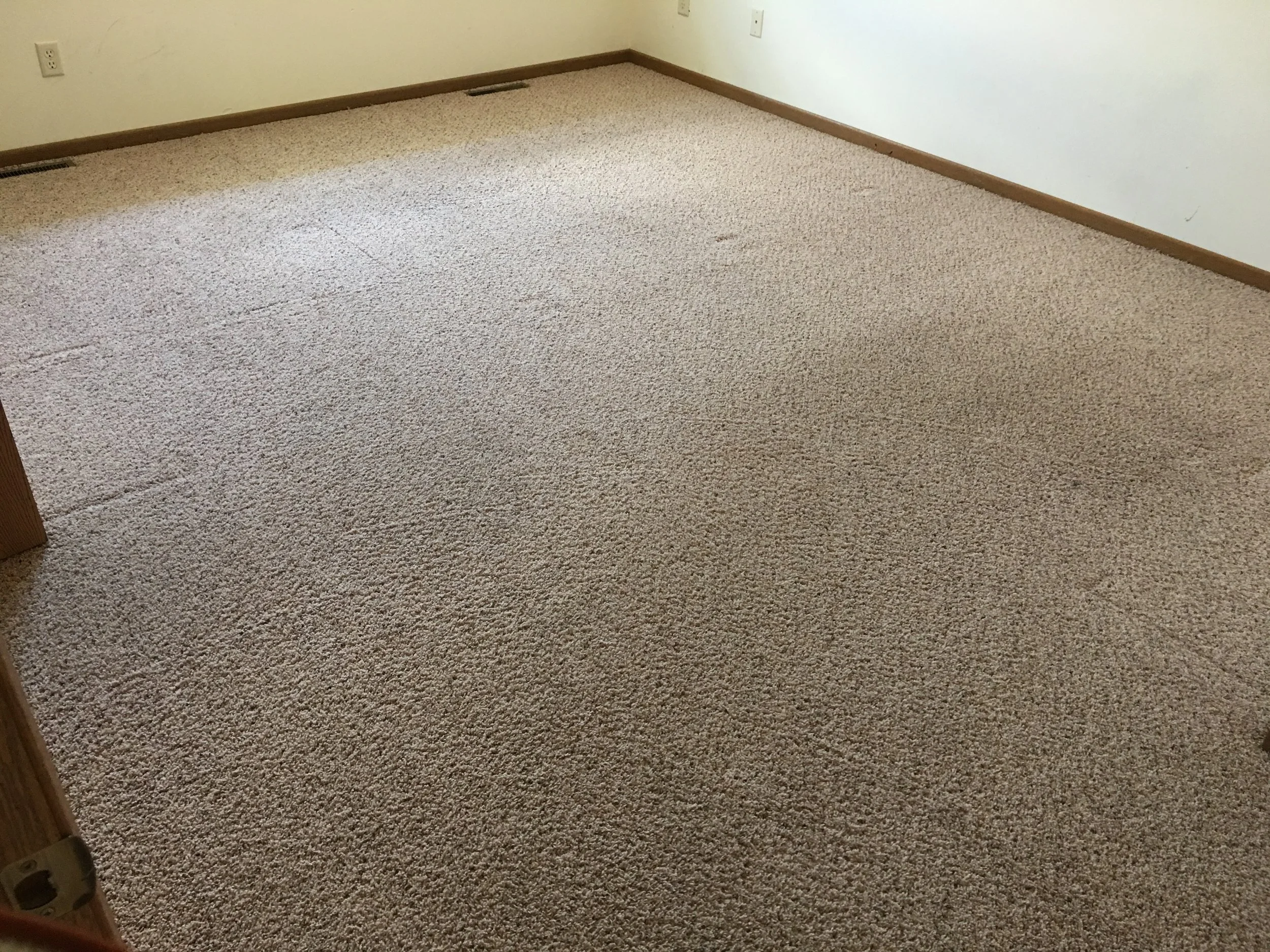 Empty room with beige carpet floor and cream walls, with electrical outlets and baseboard vents.