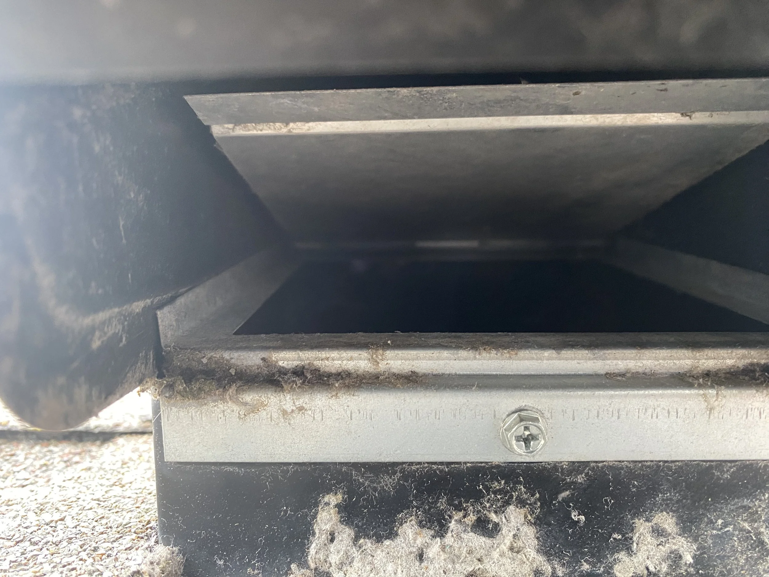 Close-up view of an empty letterbox or mail chute with metal edges, surrounded by dirt and dust.