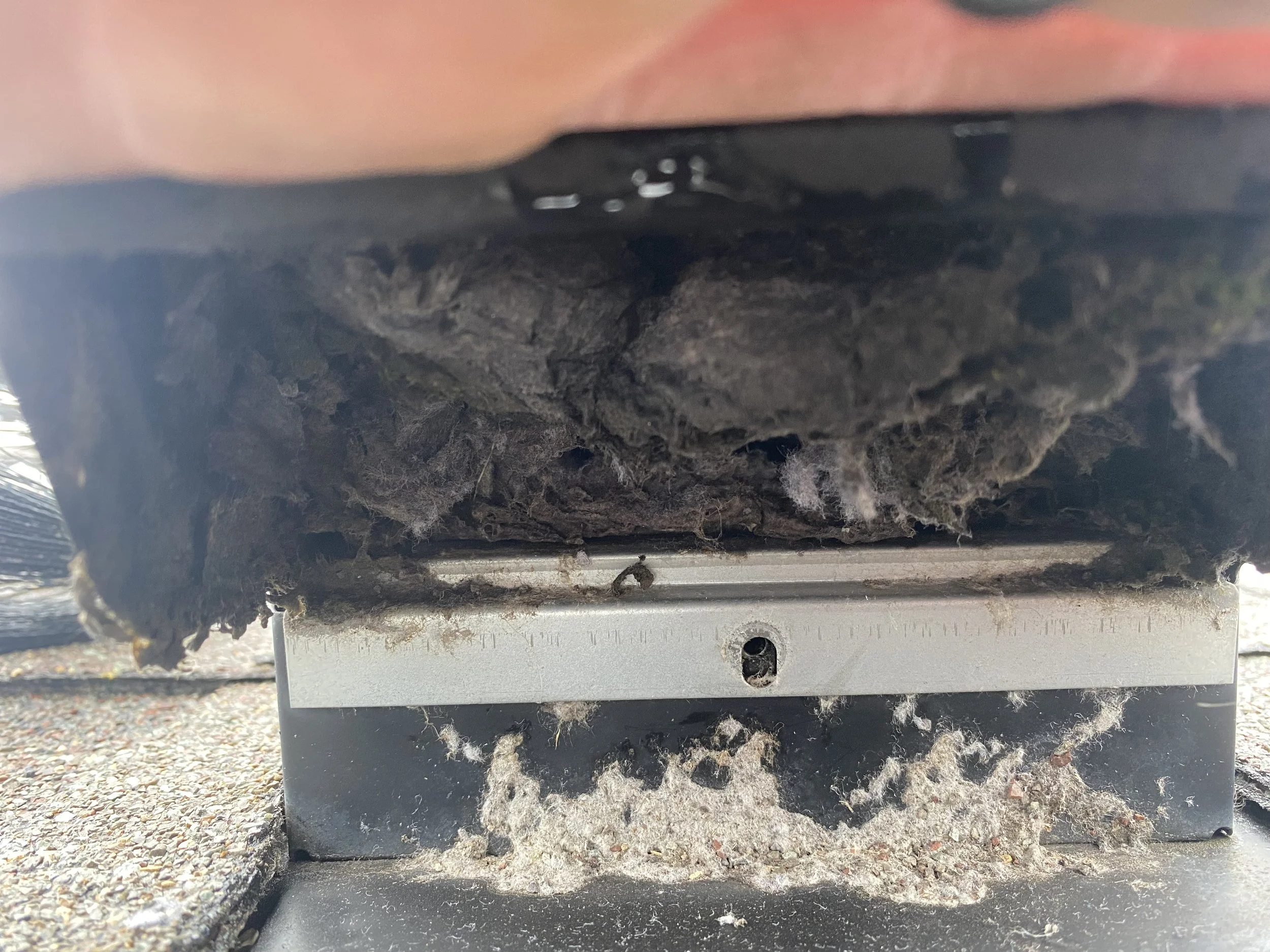 Close-up of a damaged roofing vent or exhaust fan with torn insulation and debris accumulated underneath.