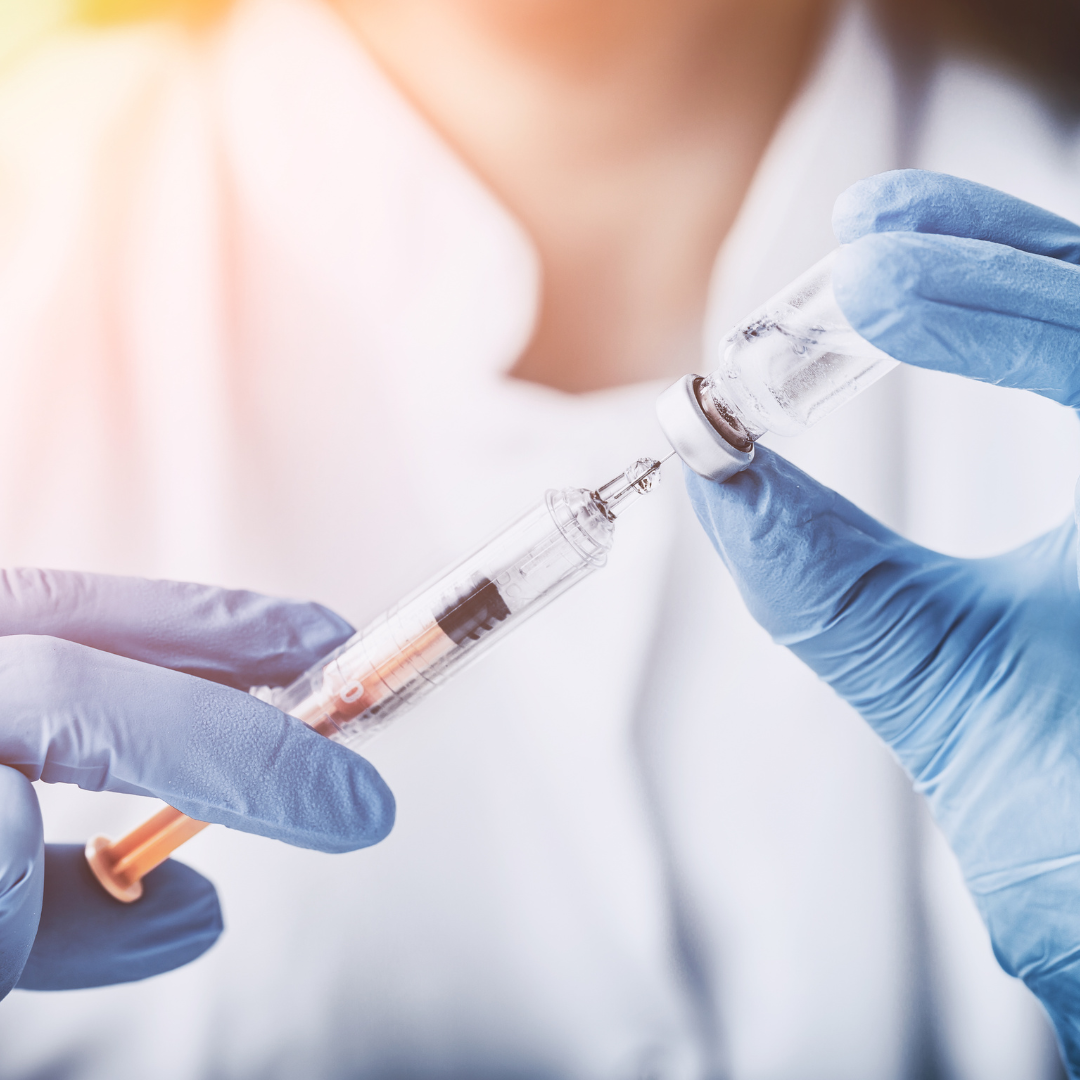 A gloved hand drawing a vitamin shot from a vial