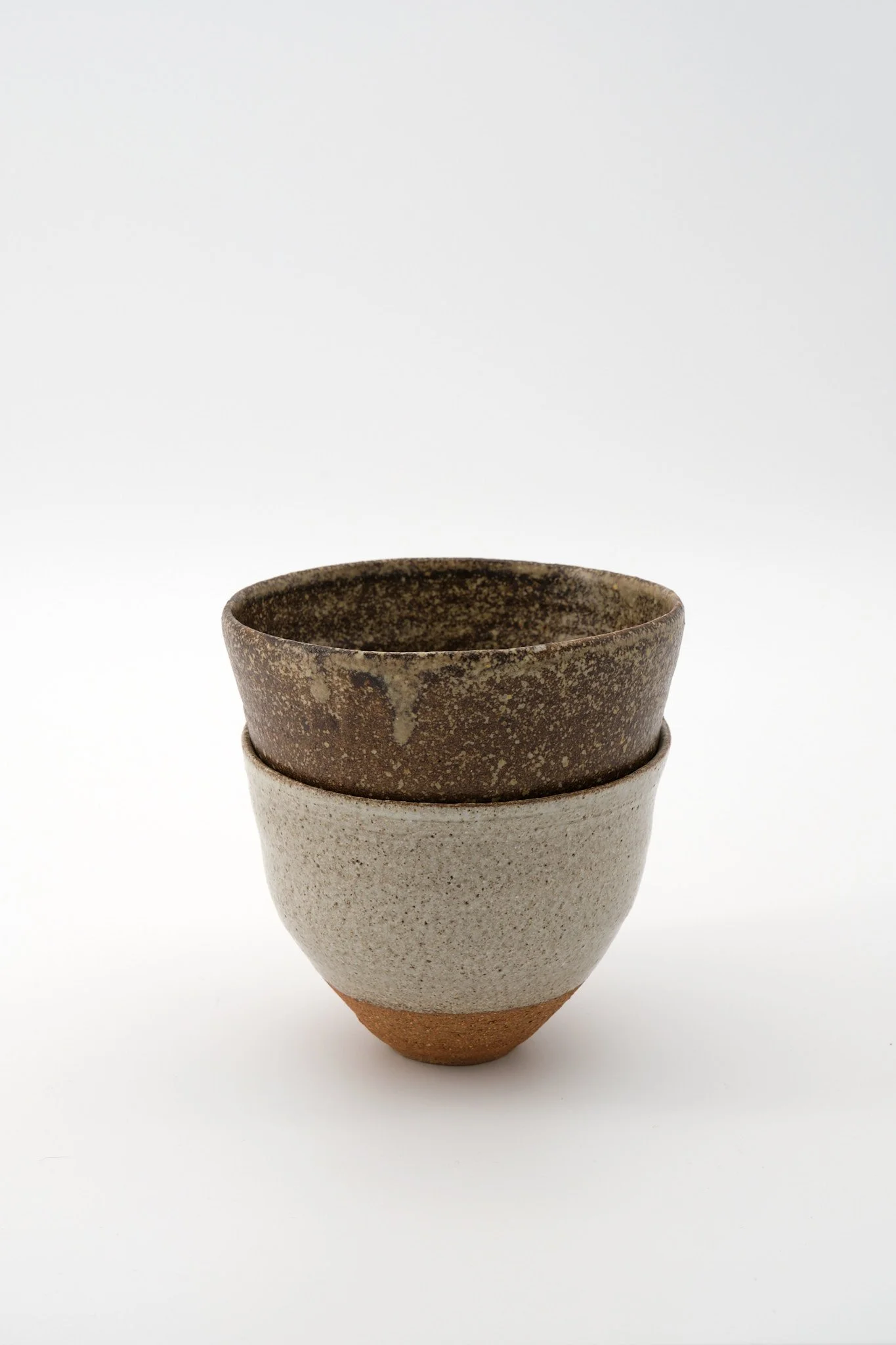 Three stacked ceramic cups with textured surfaces and earthy tones against a white background.