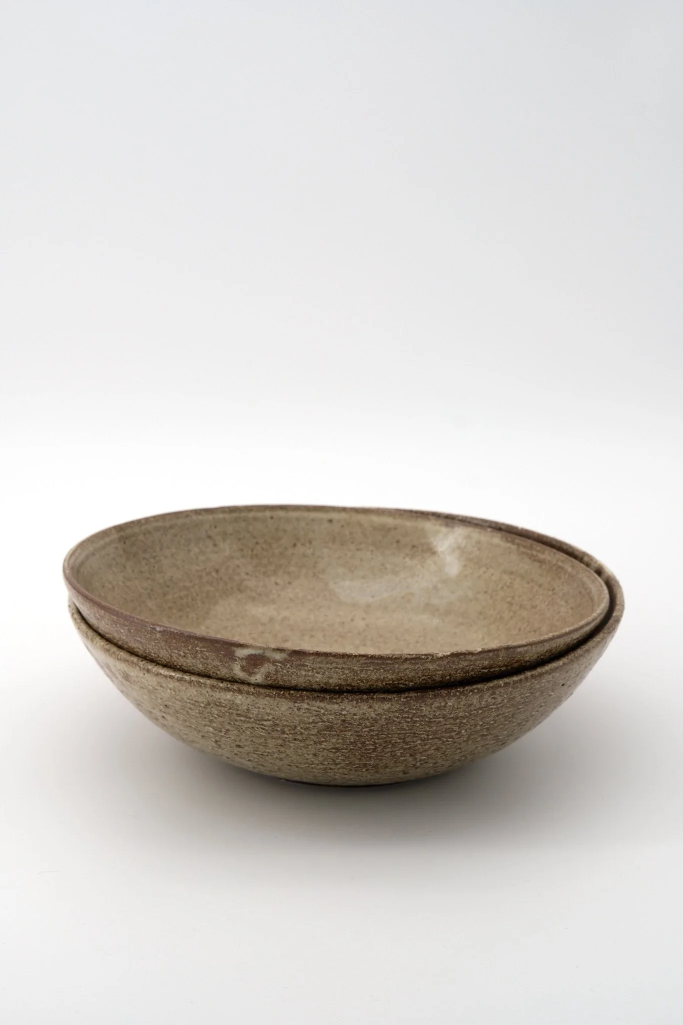 Three stacked beige, textured ceramic bowls on a white background.
