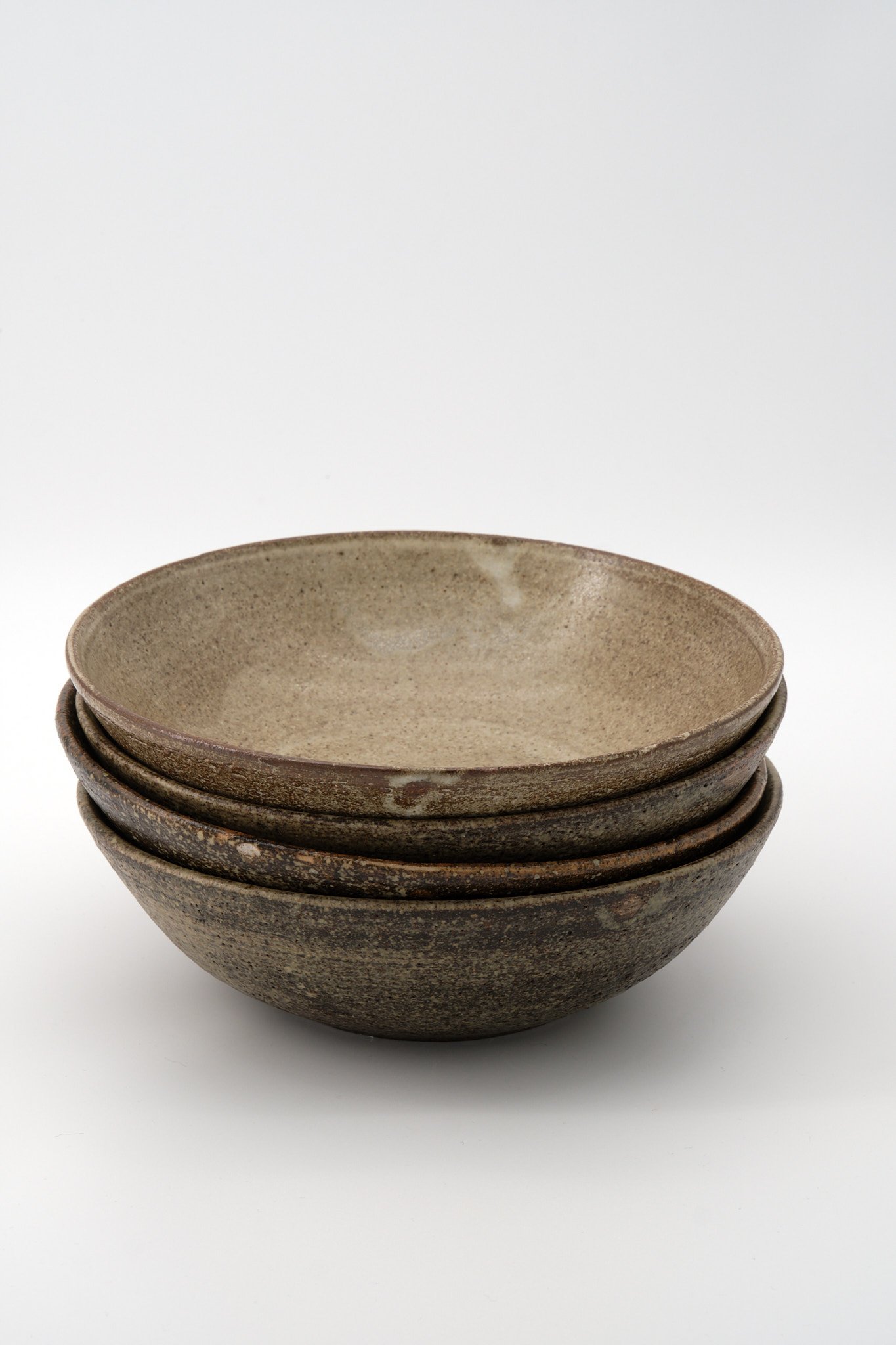 Stacked ceramic bowls in earth tones against a white background.