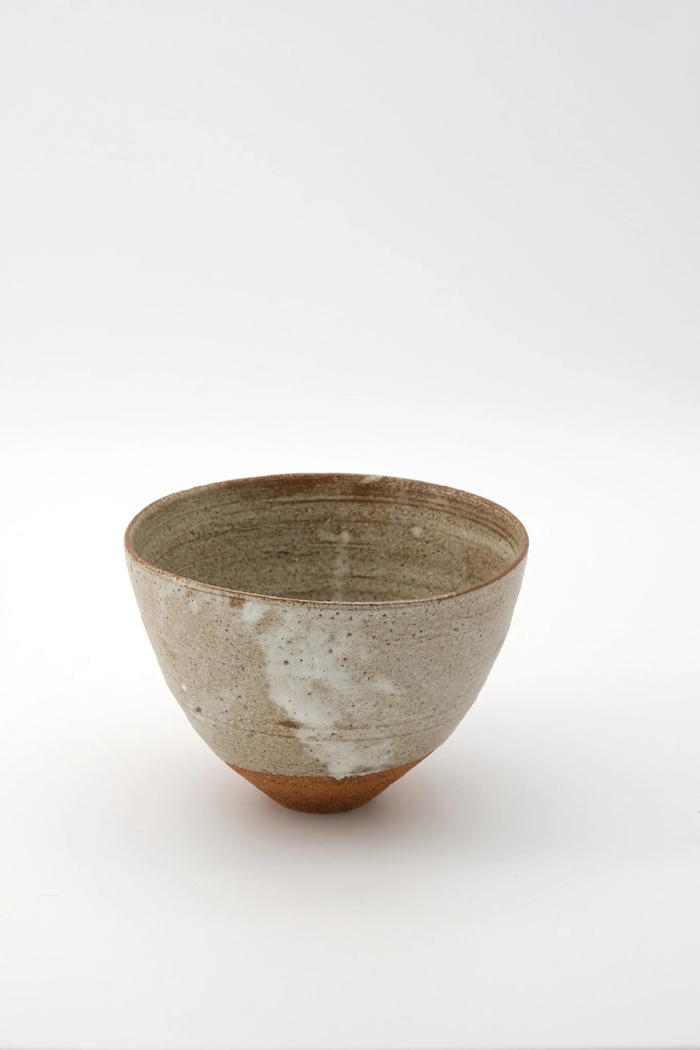 A ceramic bowl with a textured, speckled finish, displaying earthy tones of beige and brown, set against a plain white background.