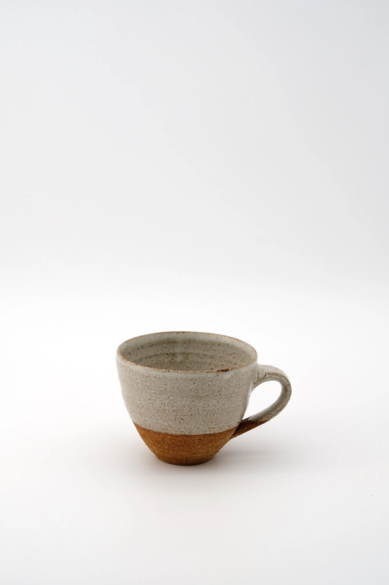 A ceramic coffee mug with a textured surface, mainly white with a brown bottom, and a curved handle, placed in front of a plain white background.