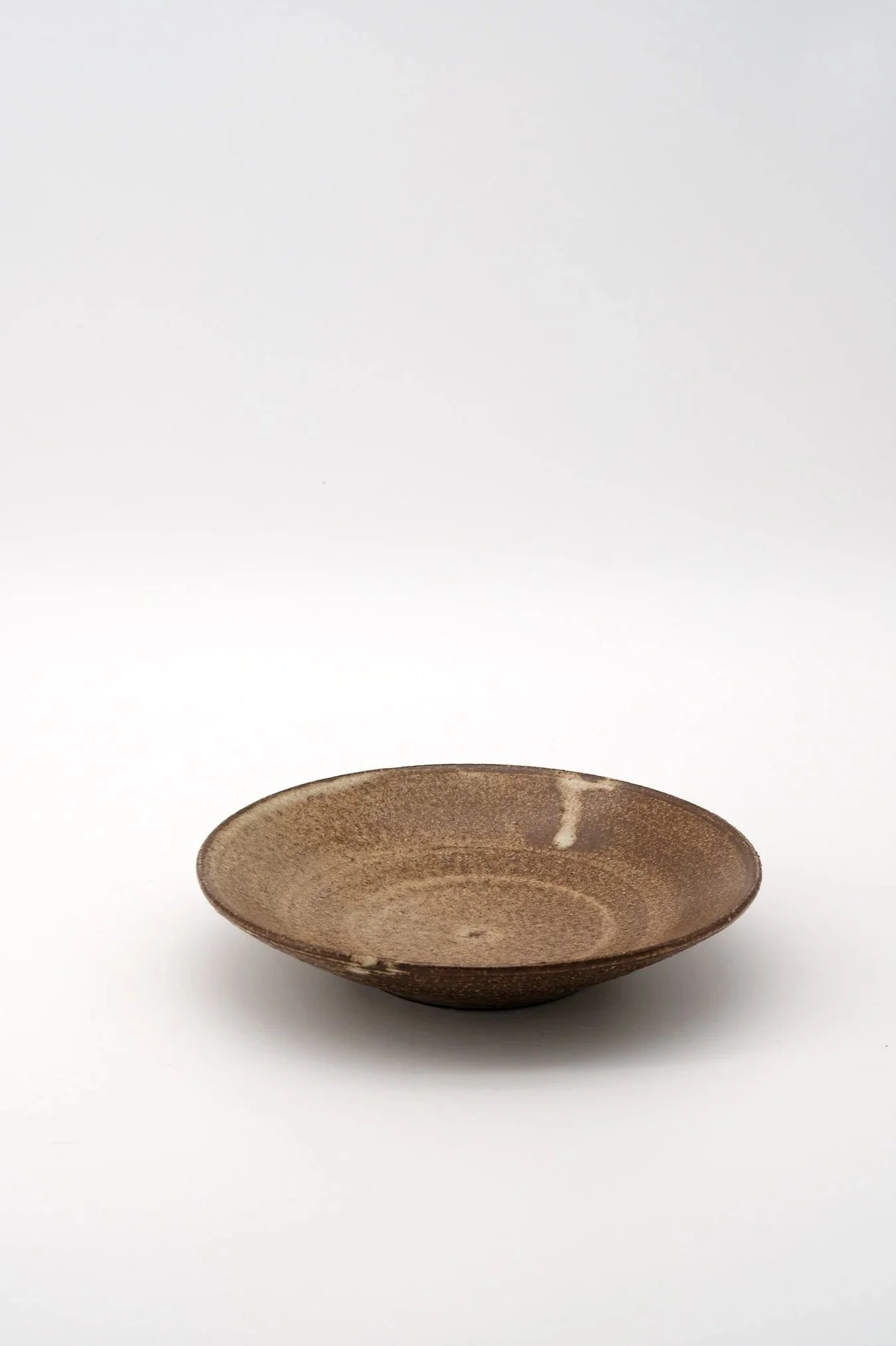 A brown ceramic bowl with a textured surface and a slightly uneven edge, placed on a white background.