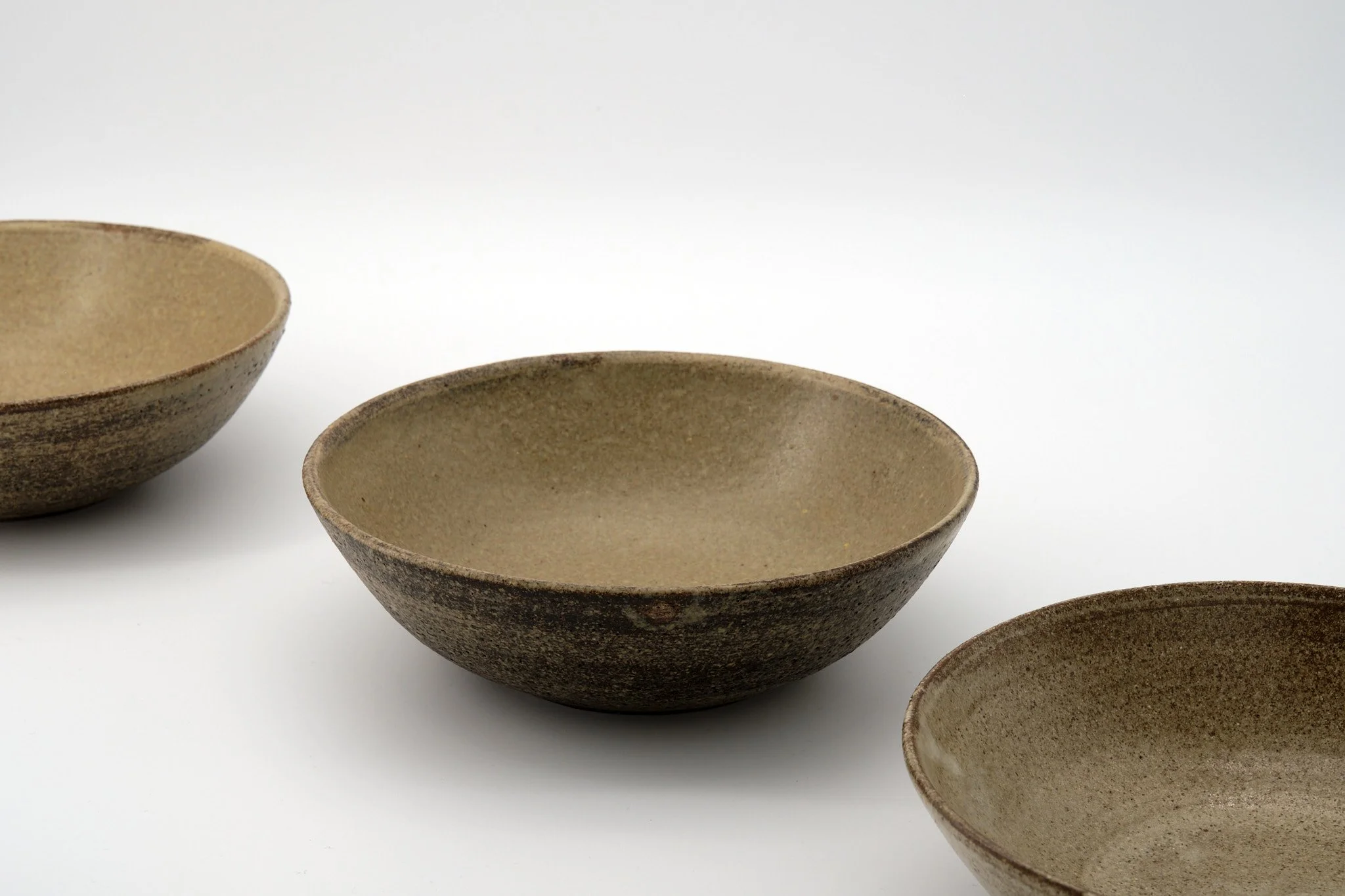 Close-up of four beige, textured ceramic bowls arranged on a white surface against a white background.