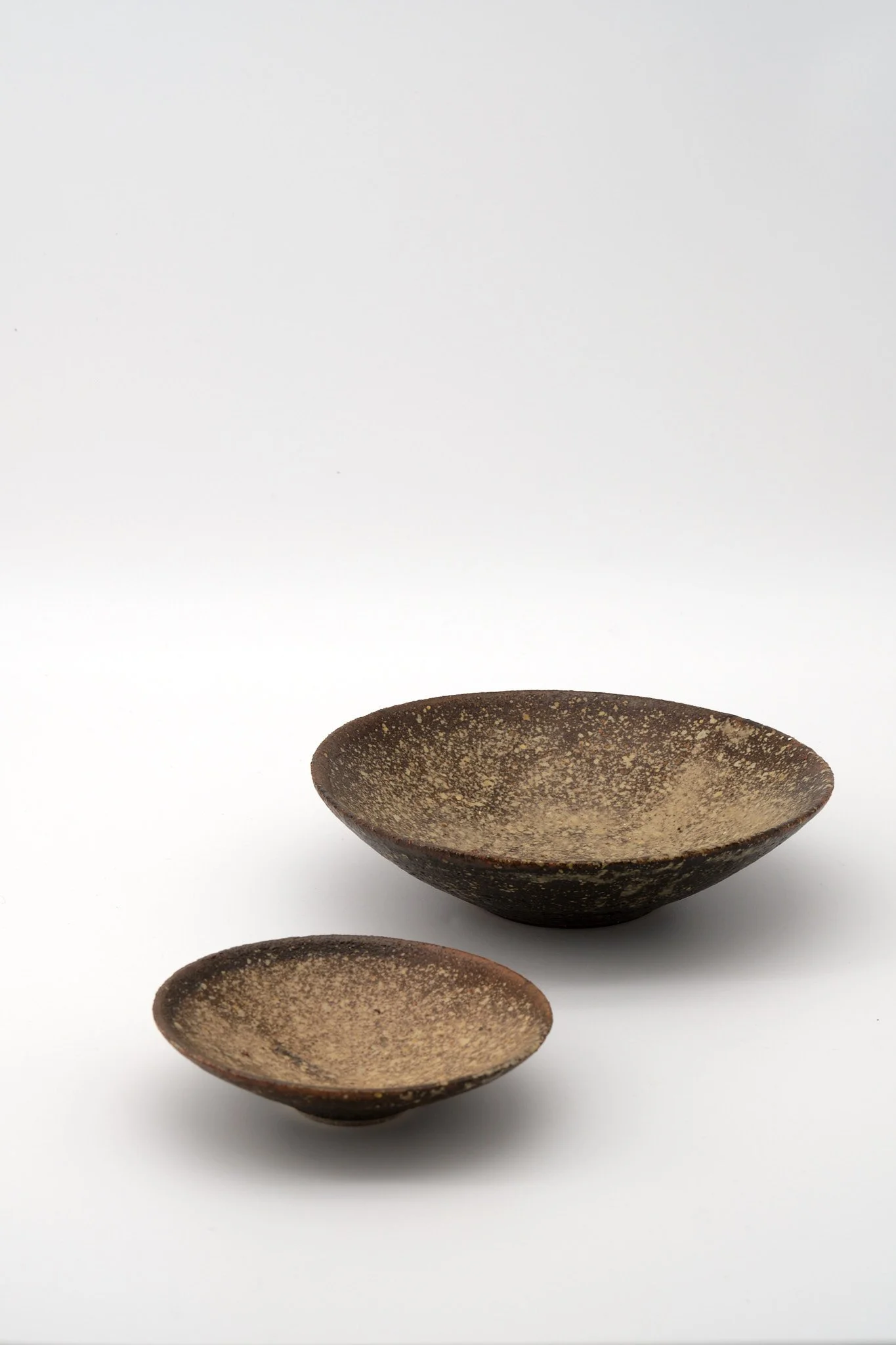 Three brown ceramic bowls with speckled glaze arranged in a descending diagonal on a white background.