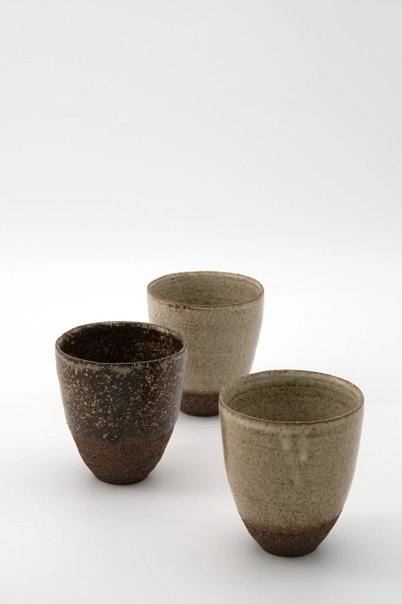 Four ceramic cups with earthy tones, arranged in a row on a white background.