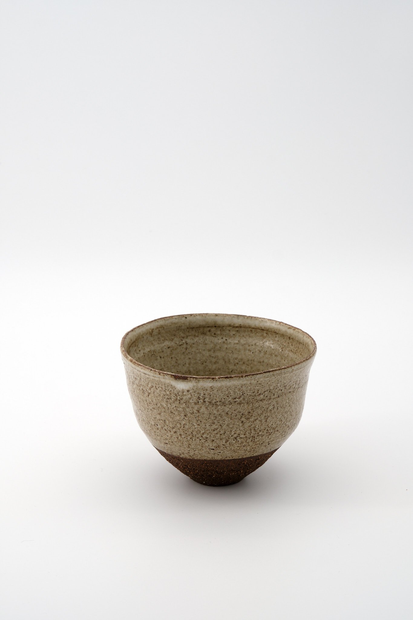 A ceramic cup with a textured surface, beige upper part, and darker, rougher bottom section, placed on a white background.