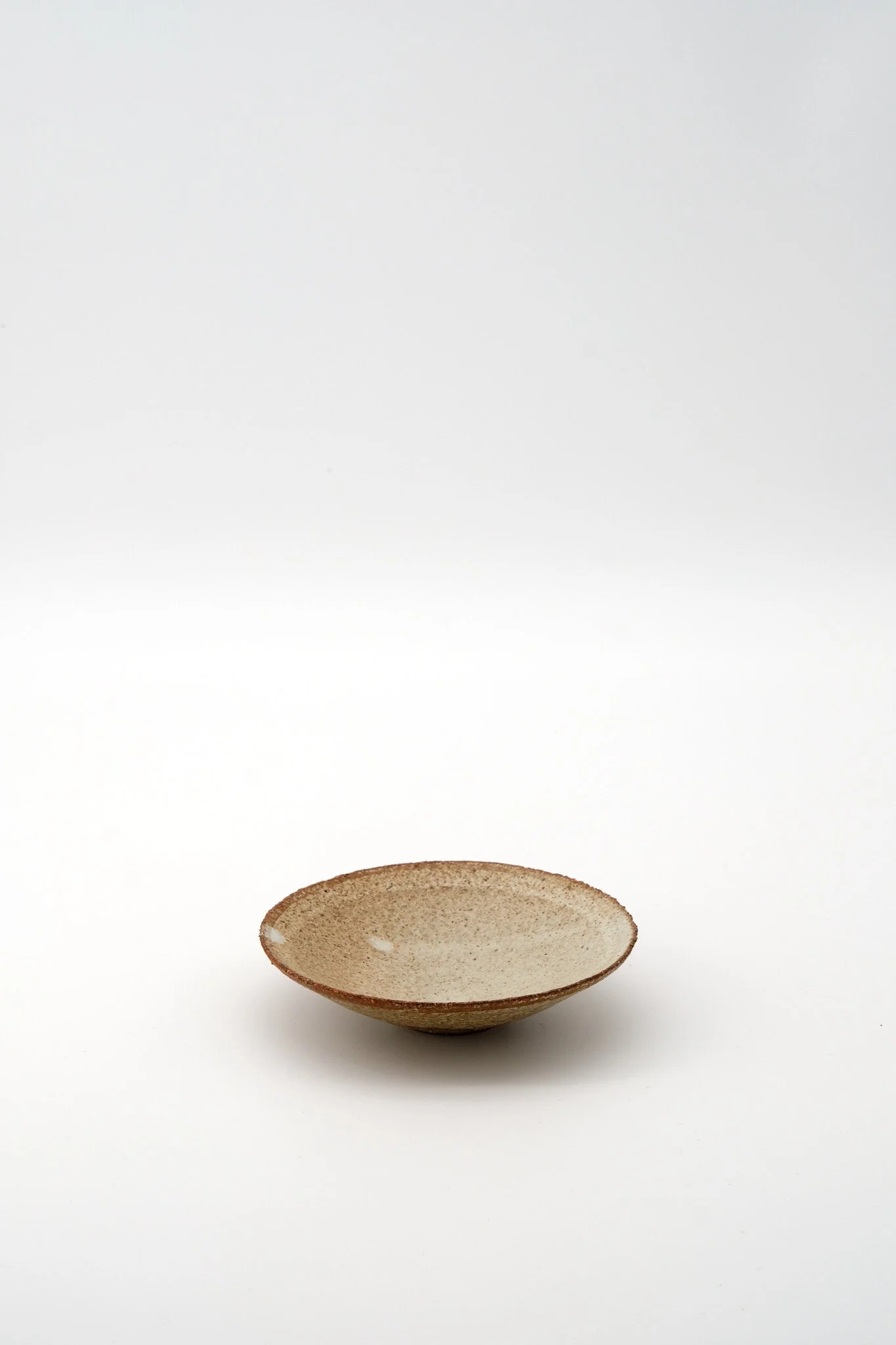 A ceramic bowl with a rough beige exterior and smooth interior, sitting on a white surface with a white background.