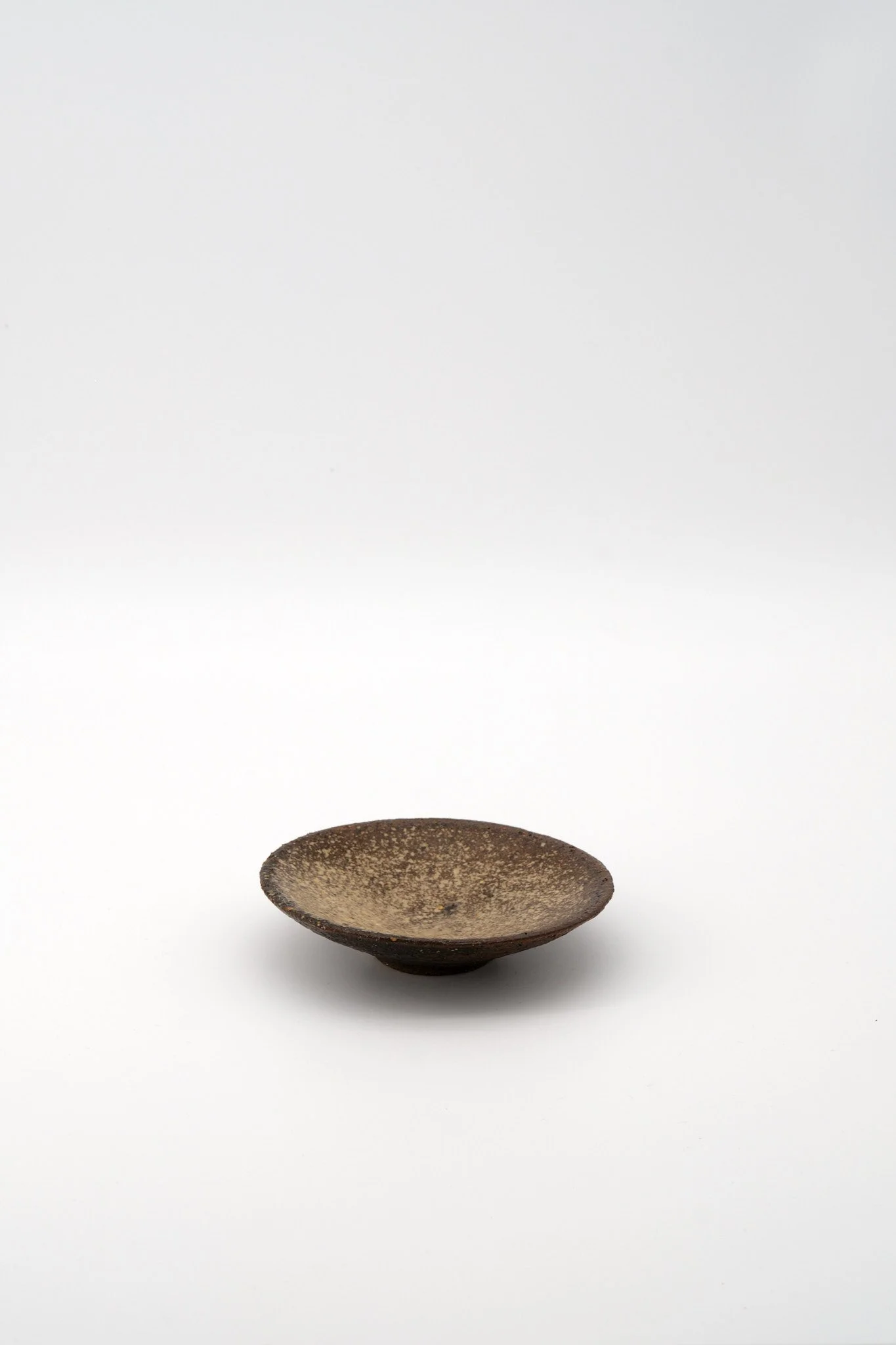 A small, dark, shallow bowl with a textured surface, placed against a plain white background.