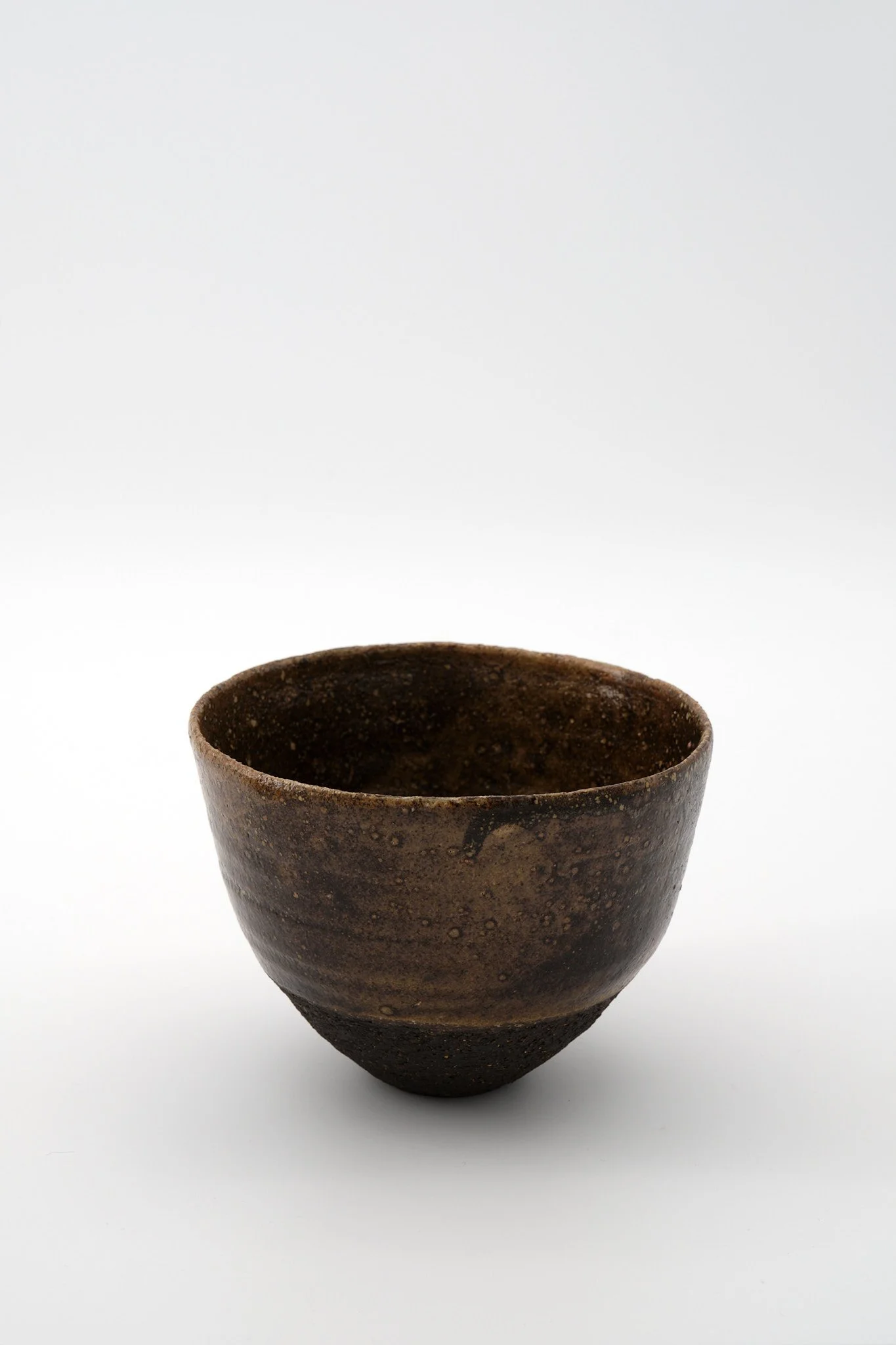 A small, round, brown ceramic cup with a slightly flared rim, decorated with subtle horizontal ridges, placed on a plain white surface.