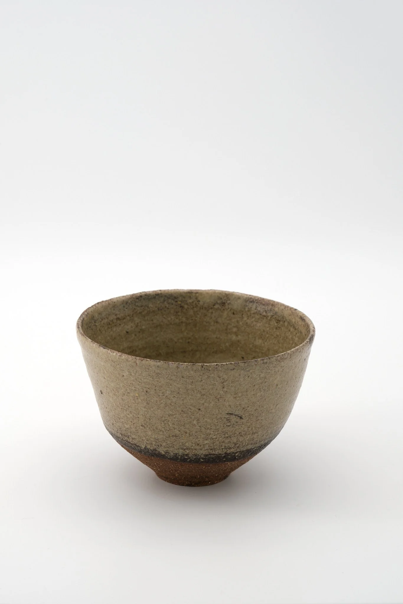 A handmade ceramic cup with a textured, speckled surface, featuring an earthy color palette, set against a plain white background.