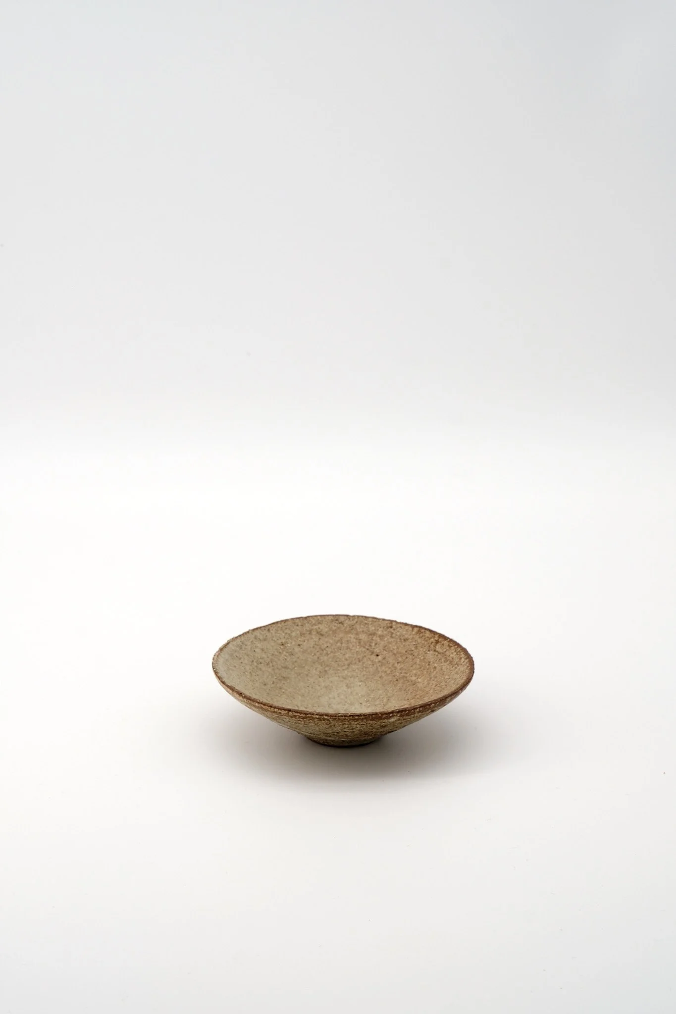 A small, shallow ceramic bowl with an earthy, textured surface, placed on a white background.