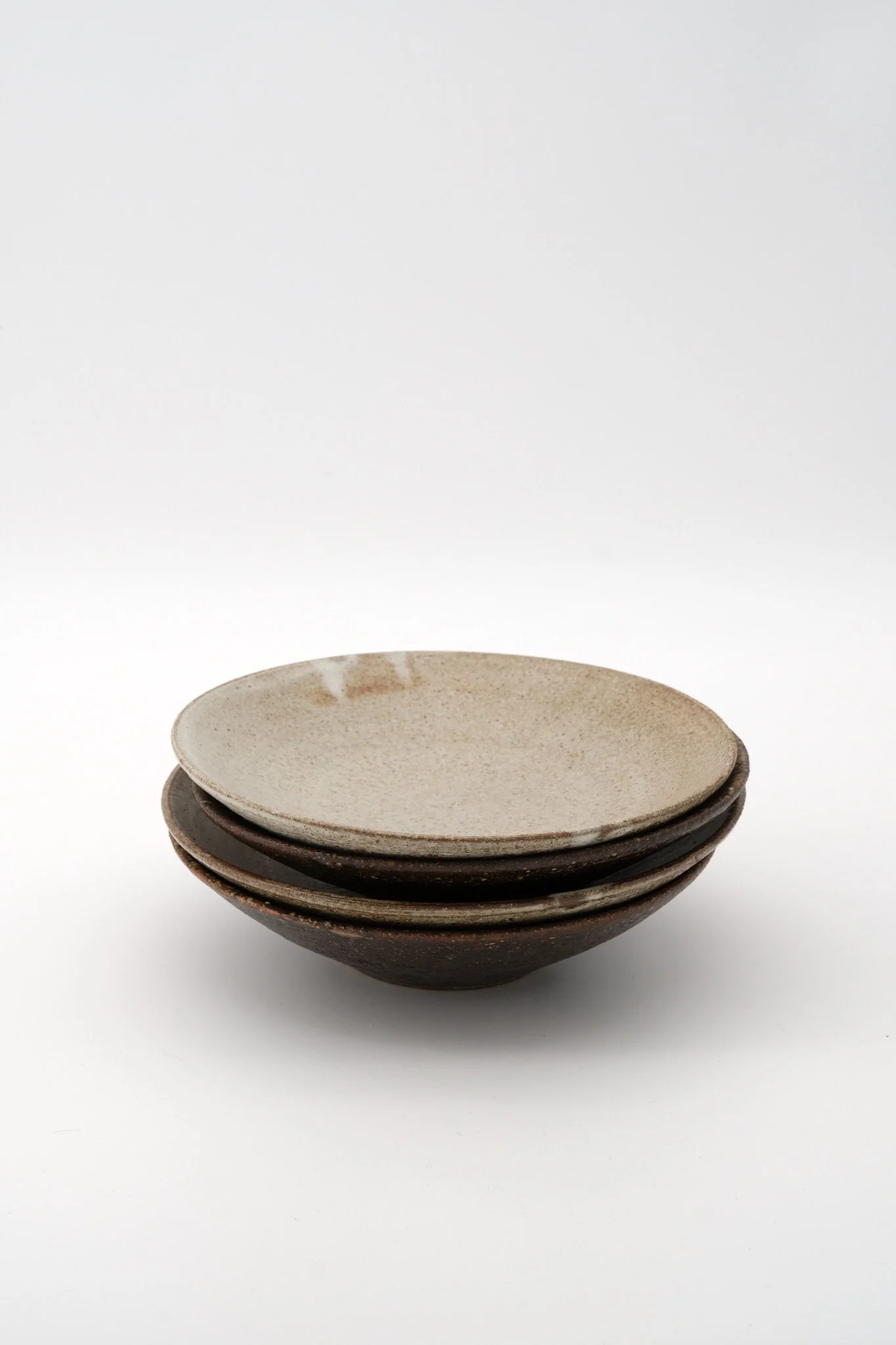Stack of four ceramic bowls with a creamy glaze on white background.