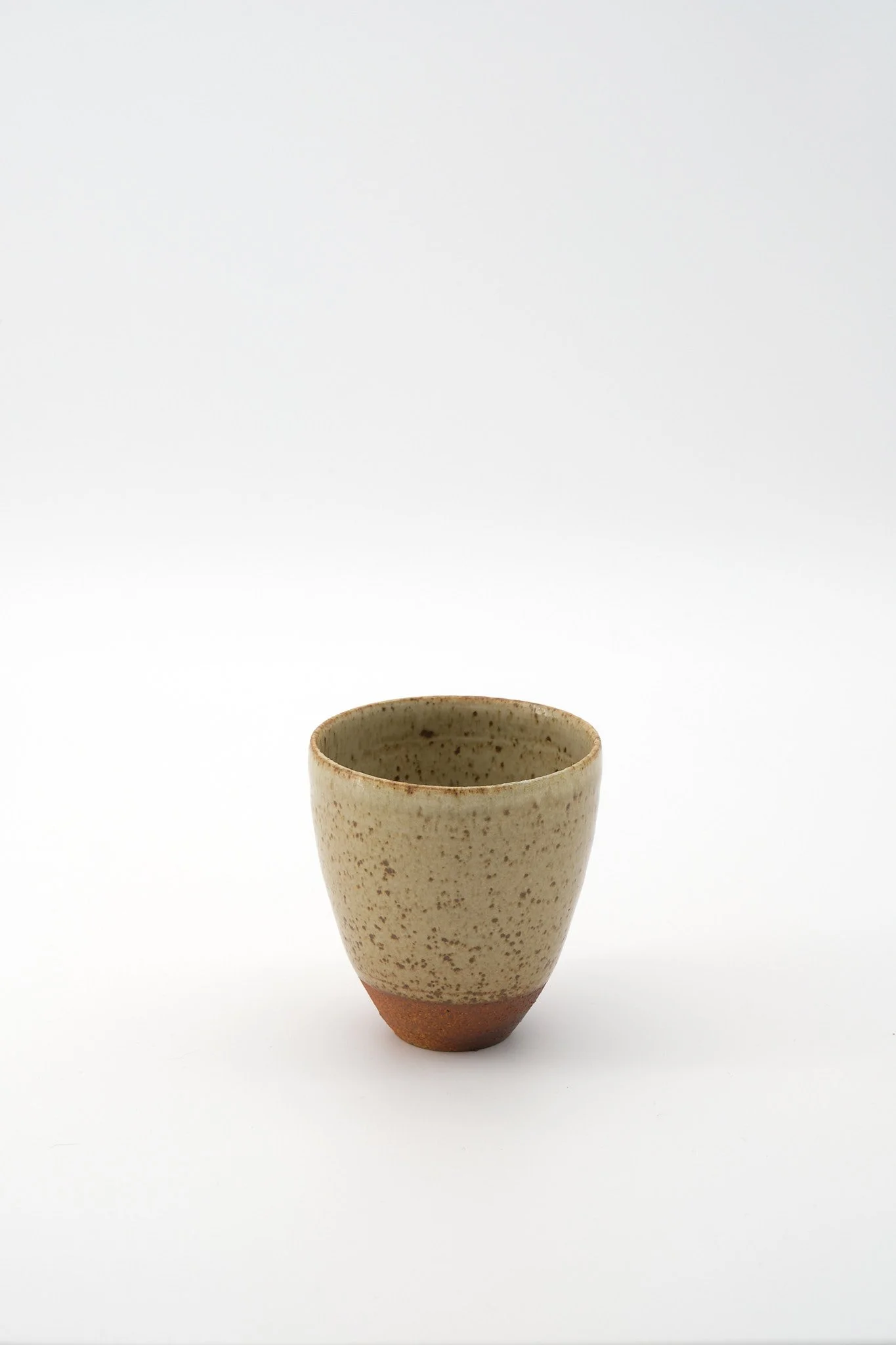 A ceramic cup with a speckled beige and brown glaze, set against a white background.