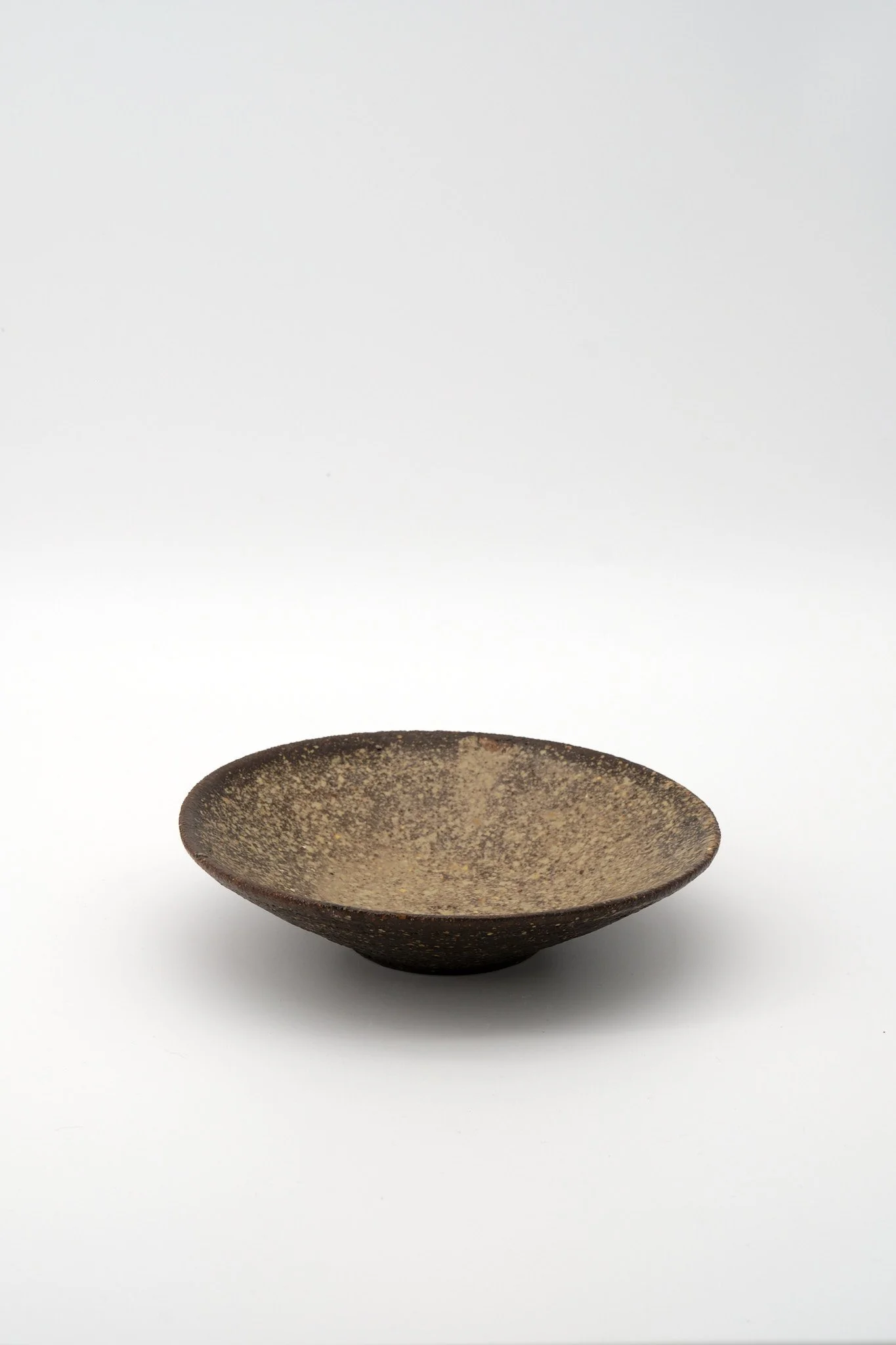 A small, dark brown ceramic bowl with a textured, speckled interior and a smooth, rounded exterior, set against a white background.