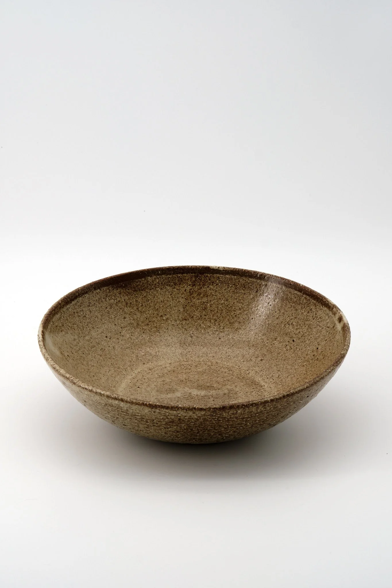 A brown, speckled ceramic bowl placed on a white surface with a plain white background.