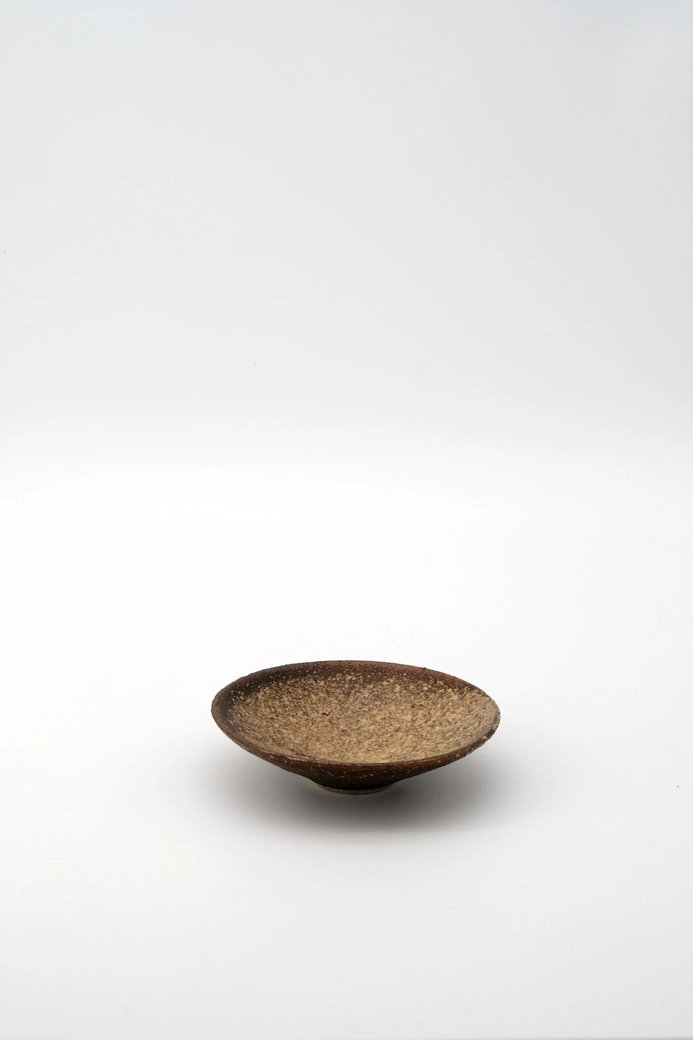 A small, round, textured, brown ceramic bowl centered on a white background.