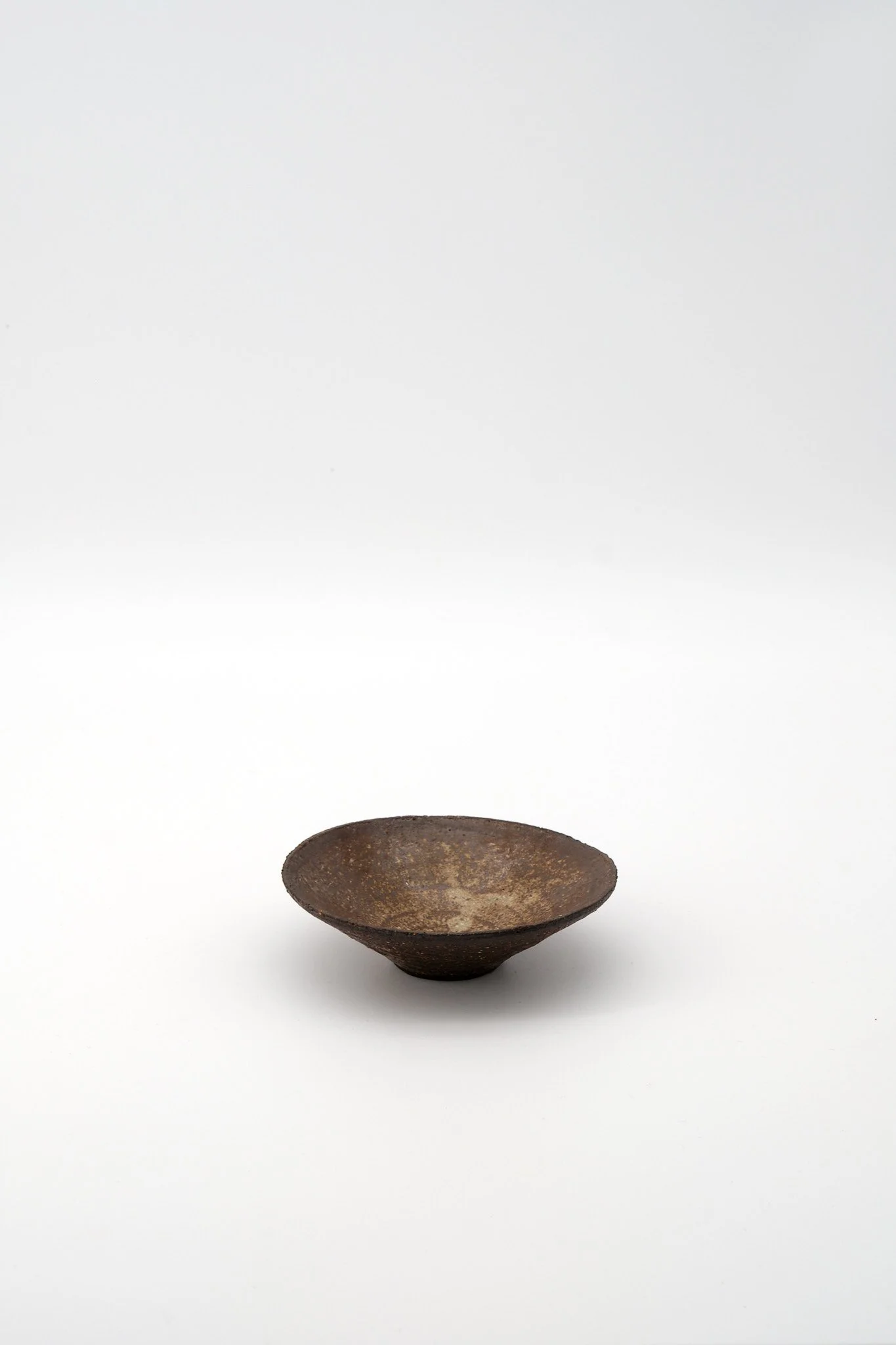 A rustic, dark brown, wide-mouthed bowl made of clay or ceramic, with a textured surface, sitting against a plain white background.
