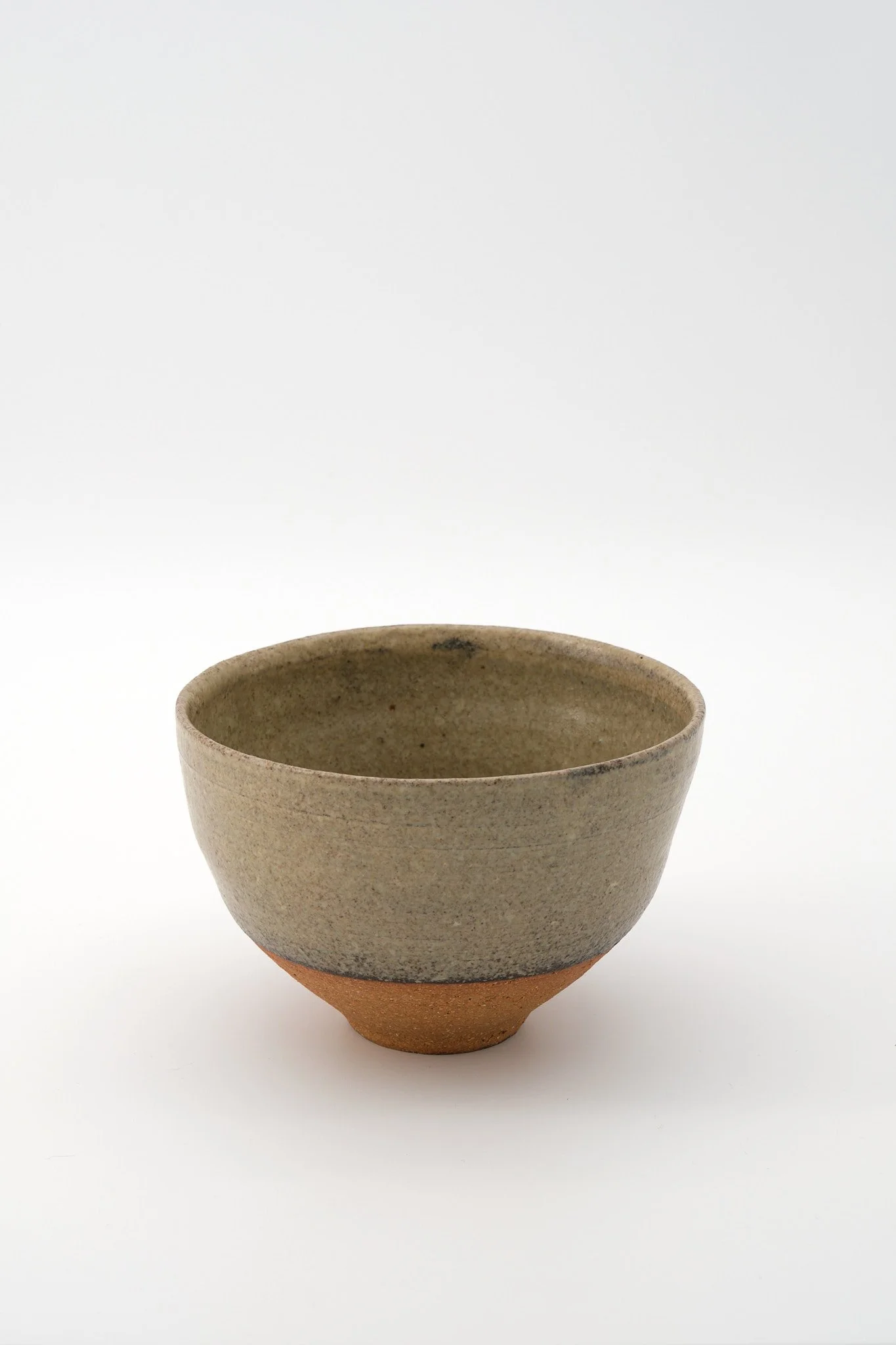 A ceramic bowl with a textured, speckled gray glaze on its interior and top, and a rough, unglazed, reddish-brown base, set against a plain white background.
