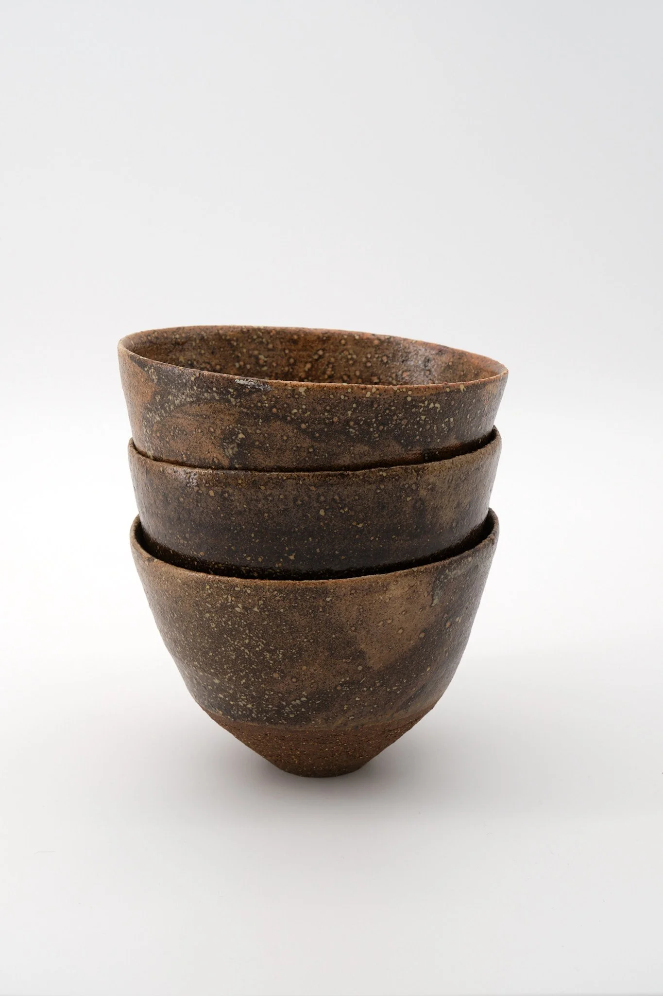 Four stacked brown ceramic bowls with speckled glaze on a white background