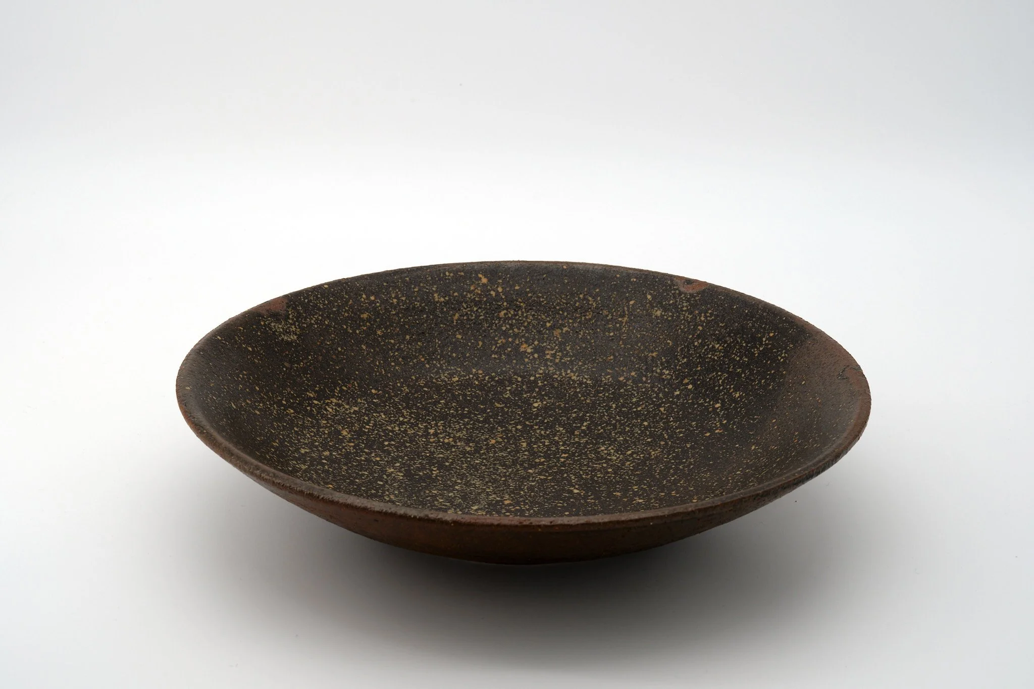 A dark ceramic bowl with a speckled pattern, seen against a plain white background.