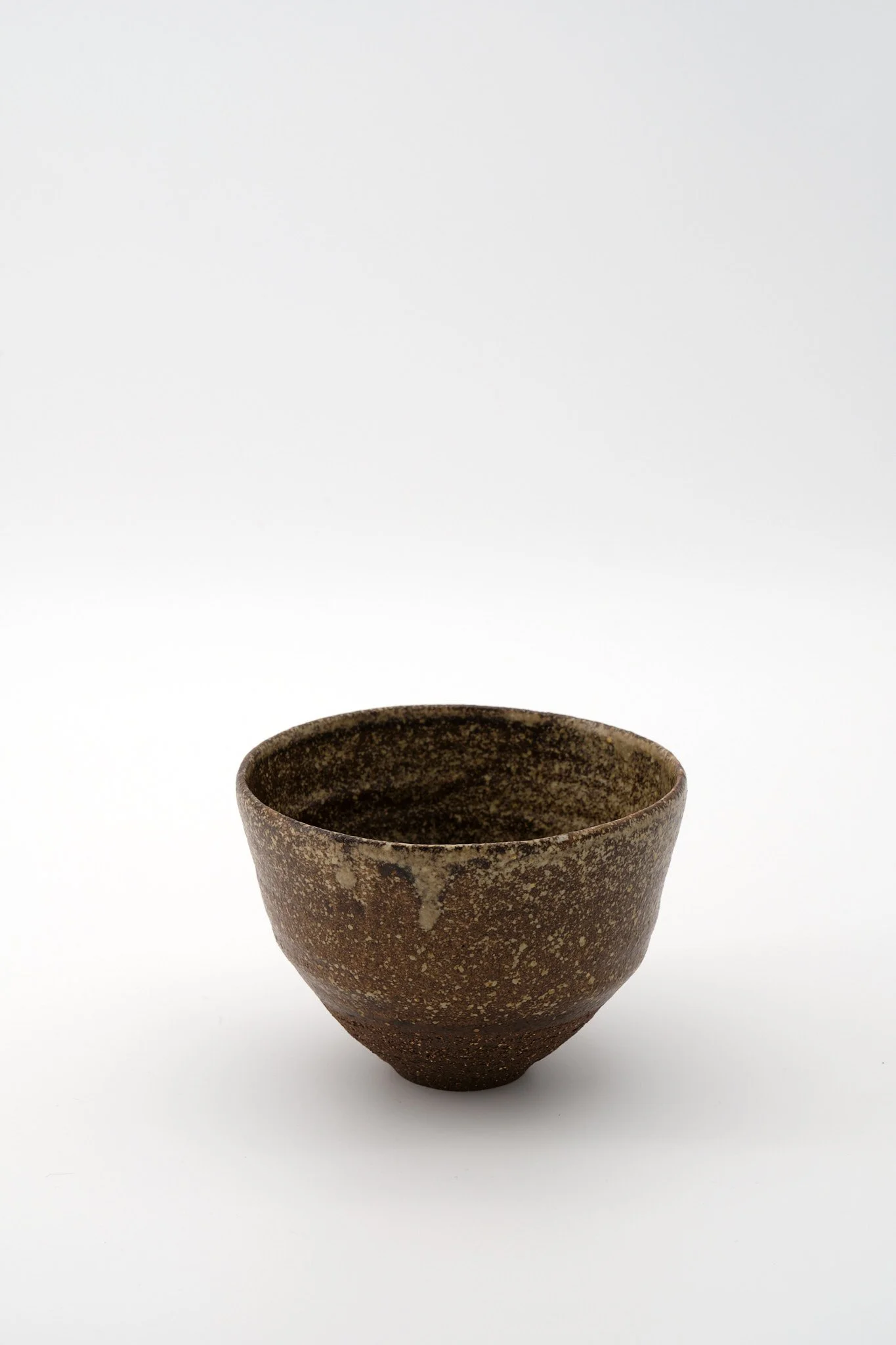 A rustic, brown ceramic bowl with a speckled texture on a white background.