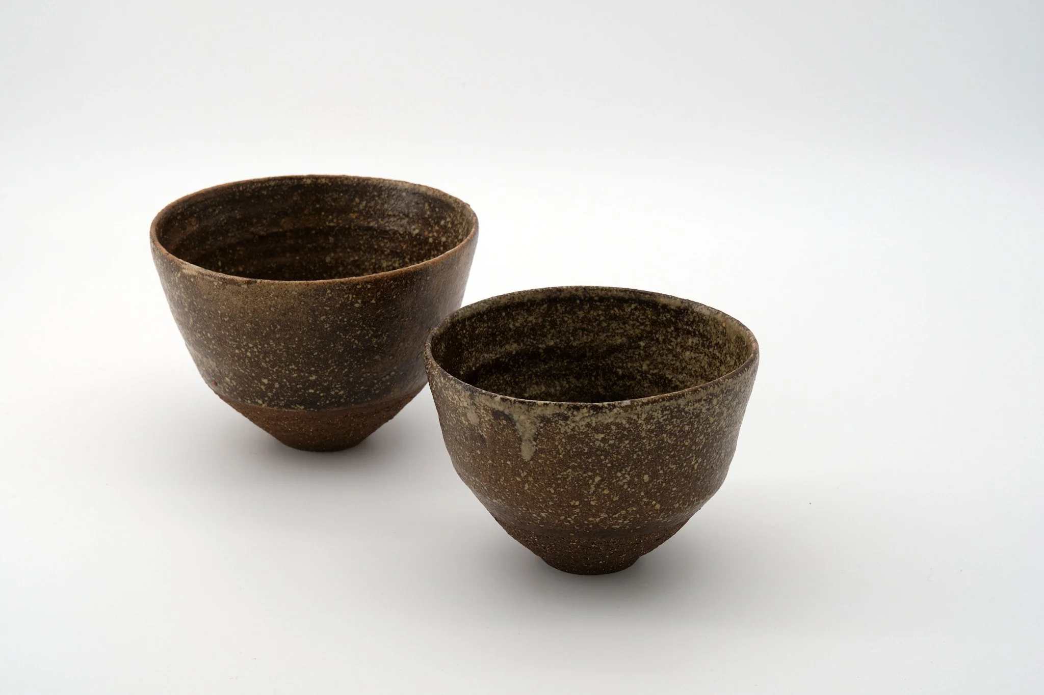 Two rustic brown ceramic bowls with speckled glaze, one larger and one smaller, positioned on a plain white background.