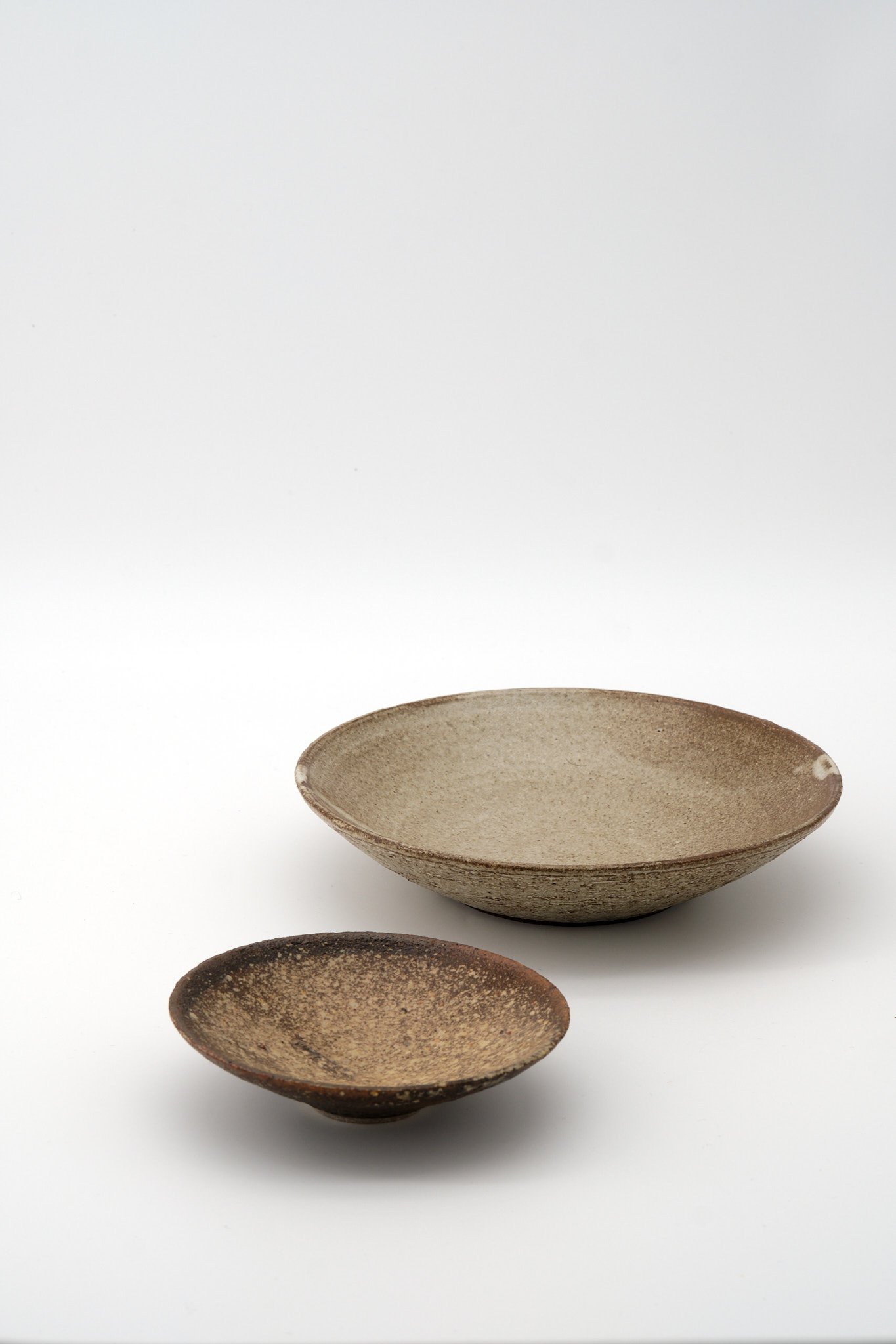 Two rustic ceramic bowls in earthy tones arranged on a white background, one filled and the other empty.