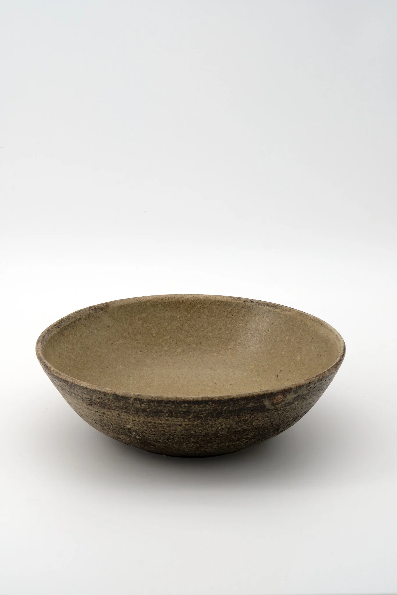 A rustic, tan ceramic bowl with a weathered appearance on a white background.