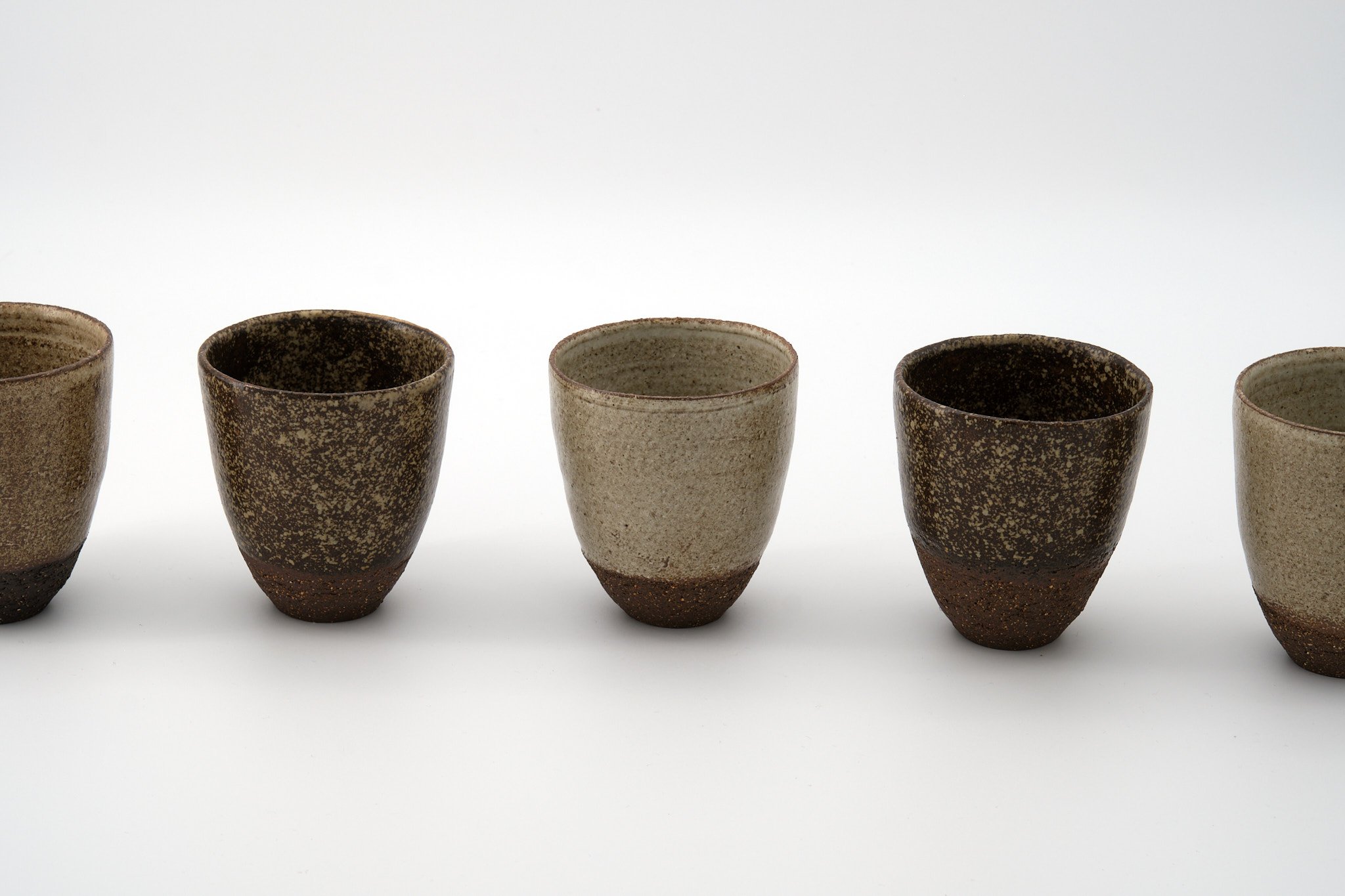 A row of five ceramic cups with a textured, earthy design against a plain light background.