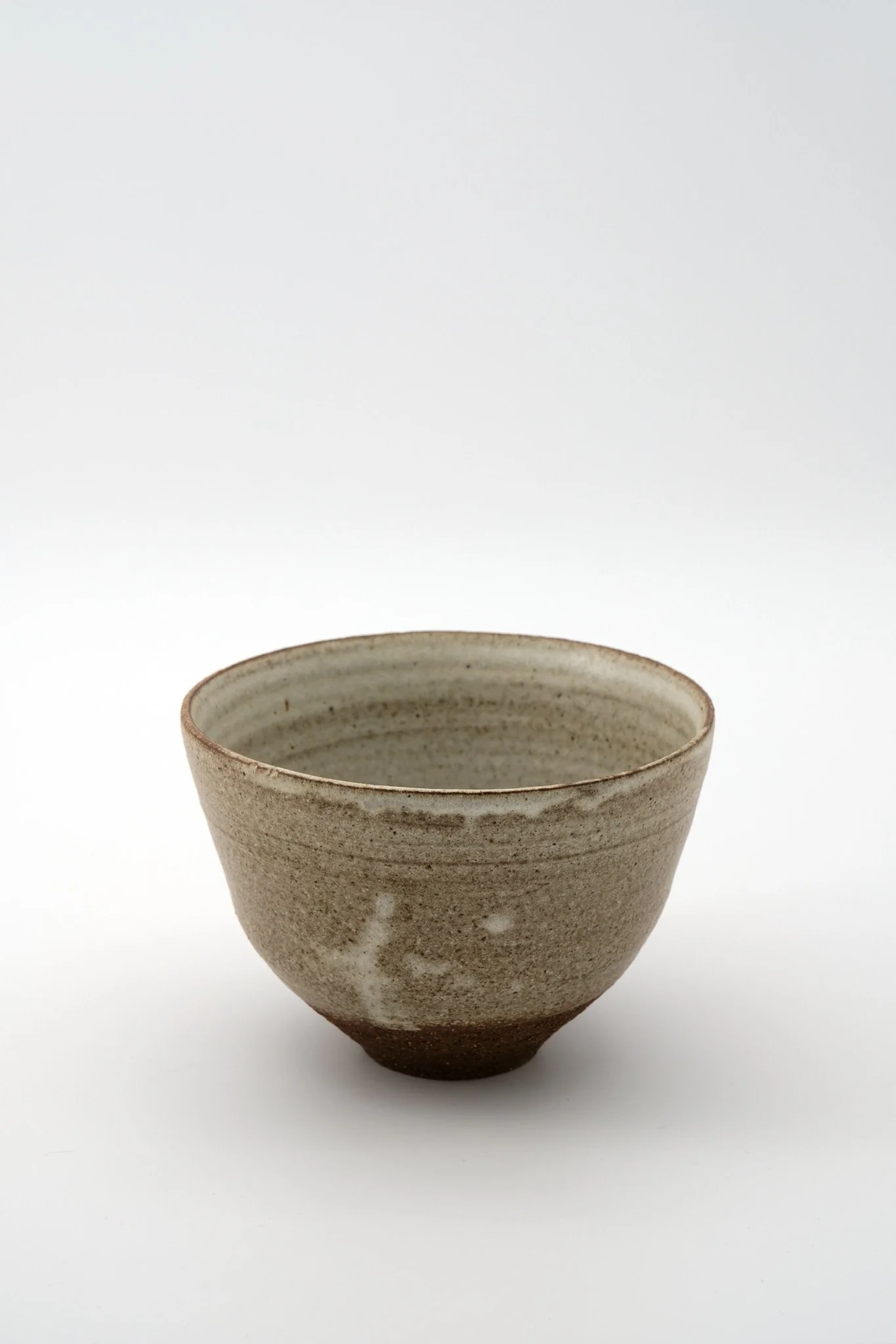 A ceramic bowl with a natural, speckled glaze and a slightly textured surface, placed against a plain white background.