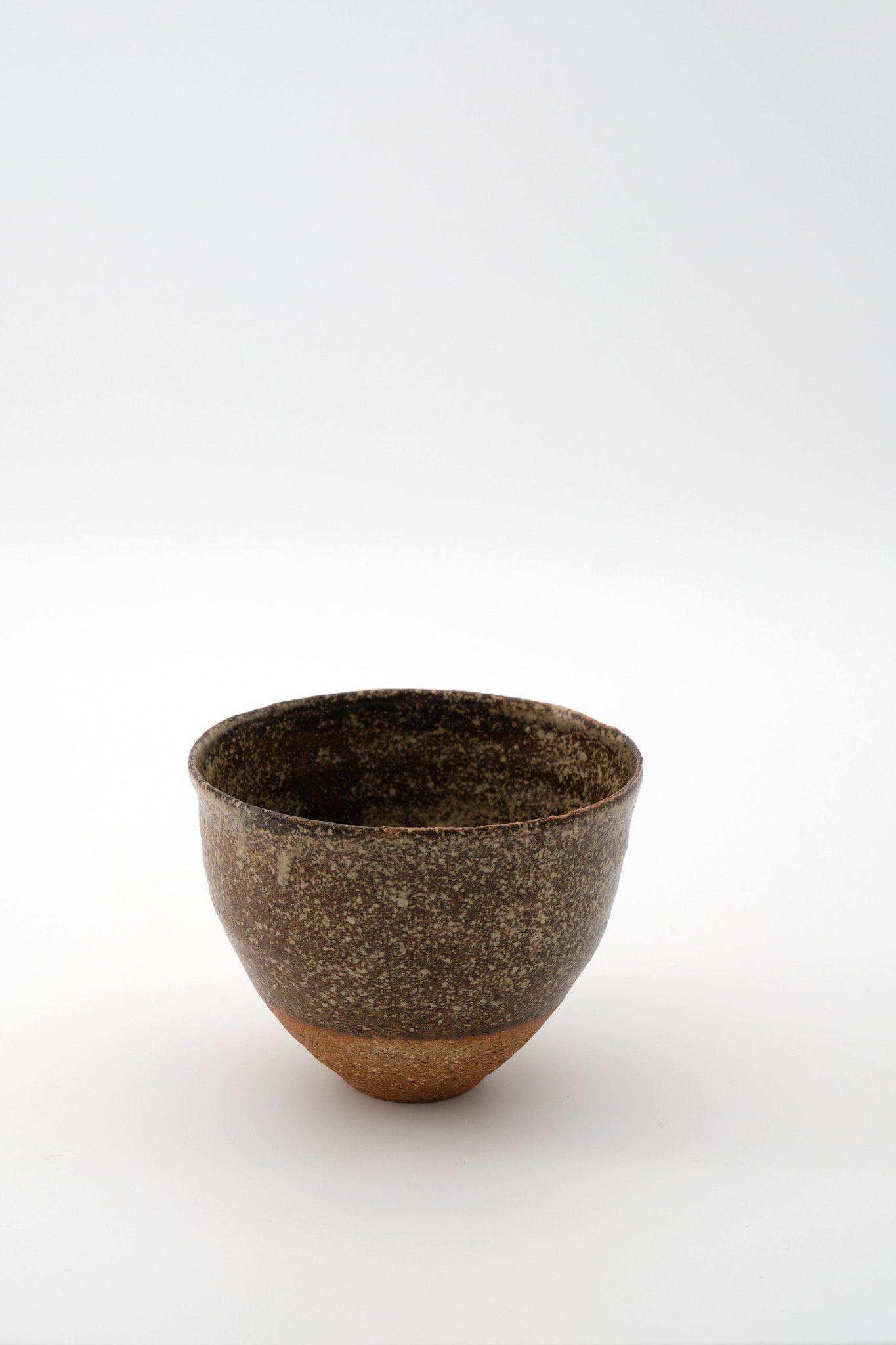 A rustic, handmade ceramic cup with a textured dark brown glaze on the outside and a smooth, reddish-brown base, set against a plain white background.