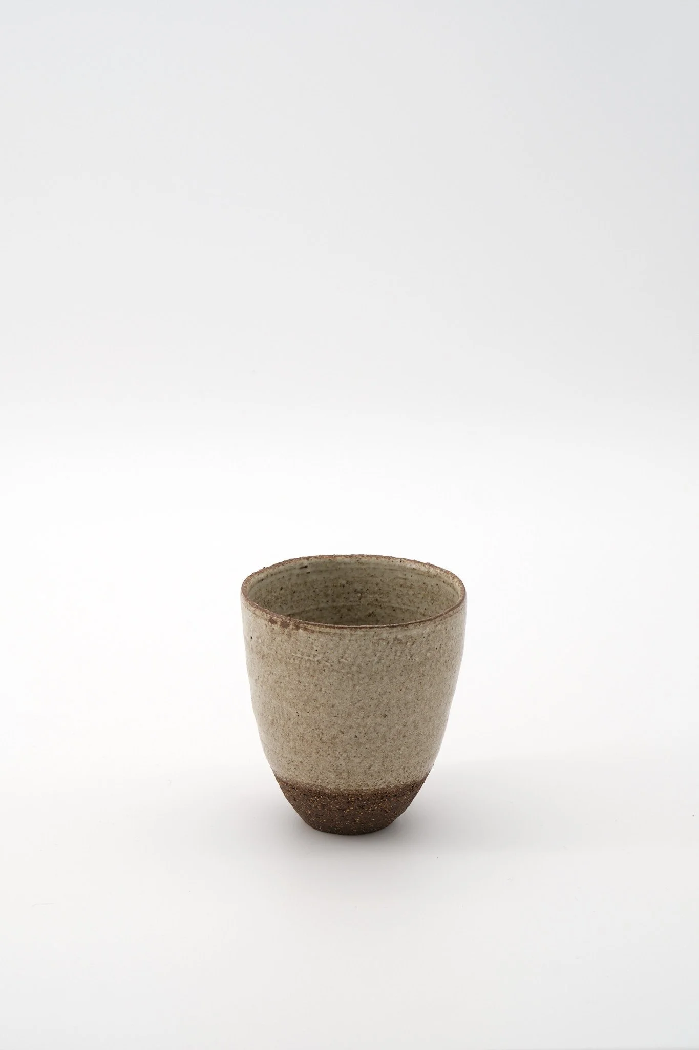 A ceramic cup with a rough, textured surface, tapering off at the bottom, on a white background.