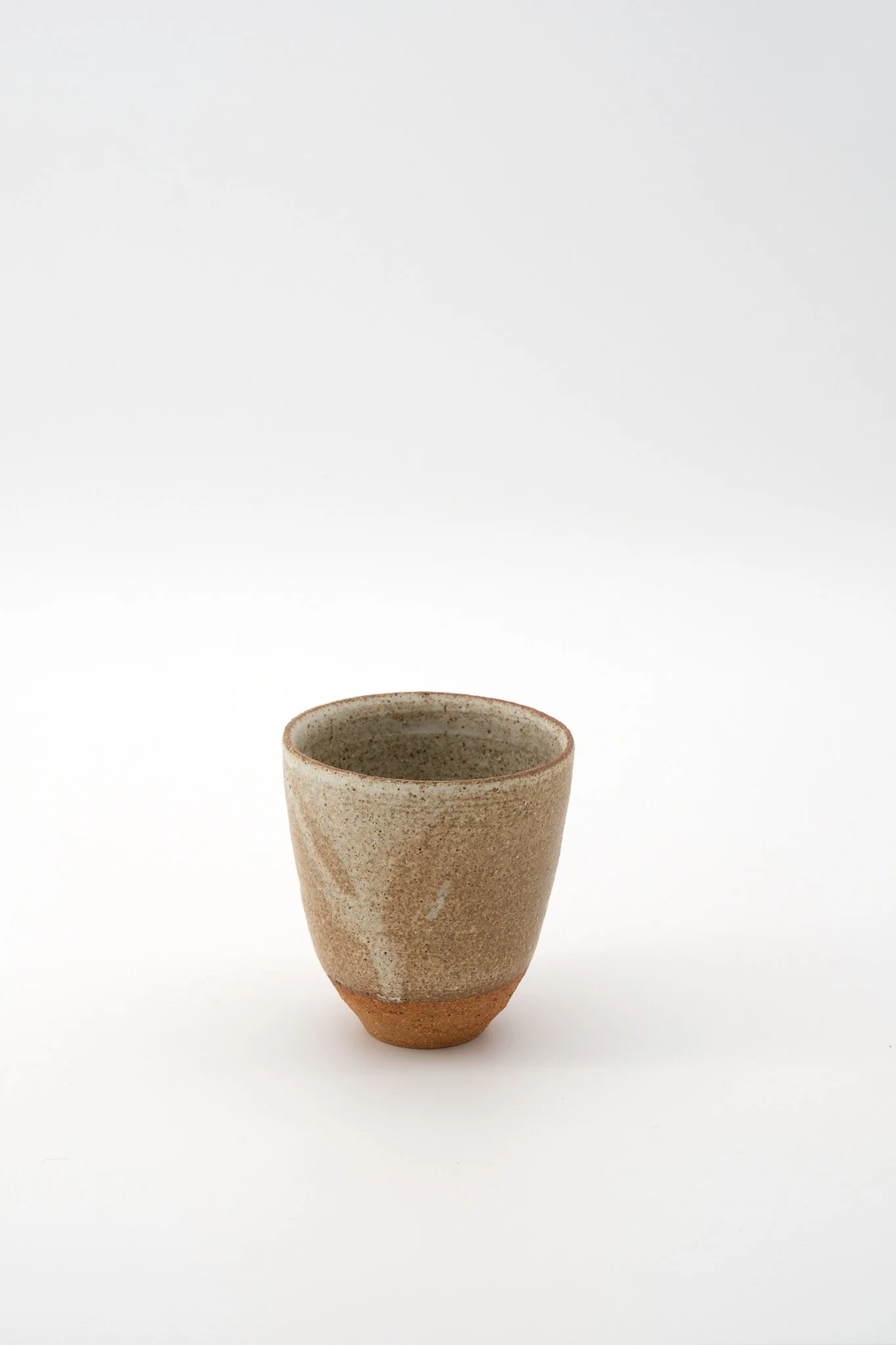 A ceramic cup with a textured, earthy appearance, featuring a speckled glaze and a terracotta-colored base, set against a plain white background.
