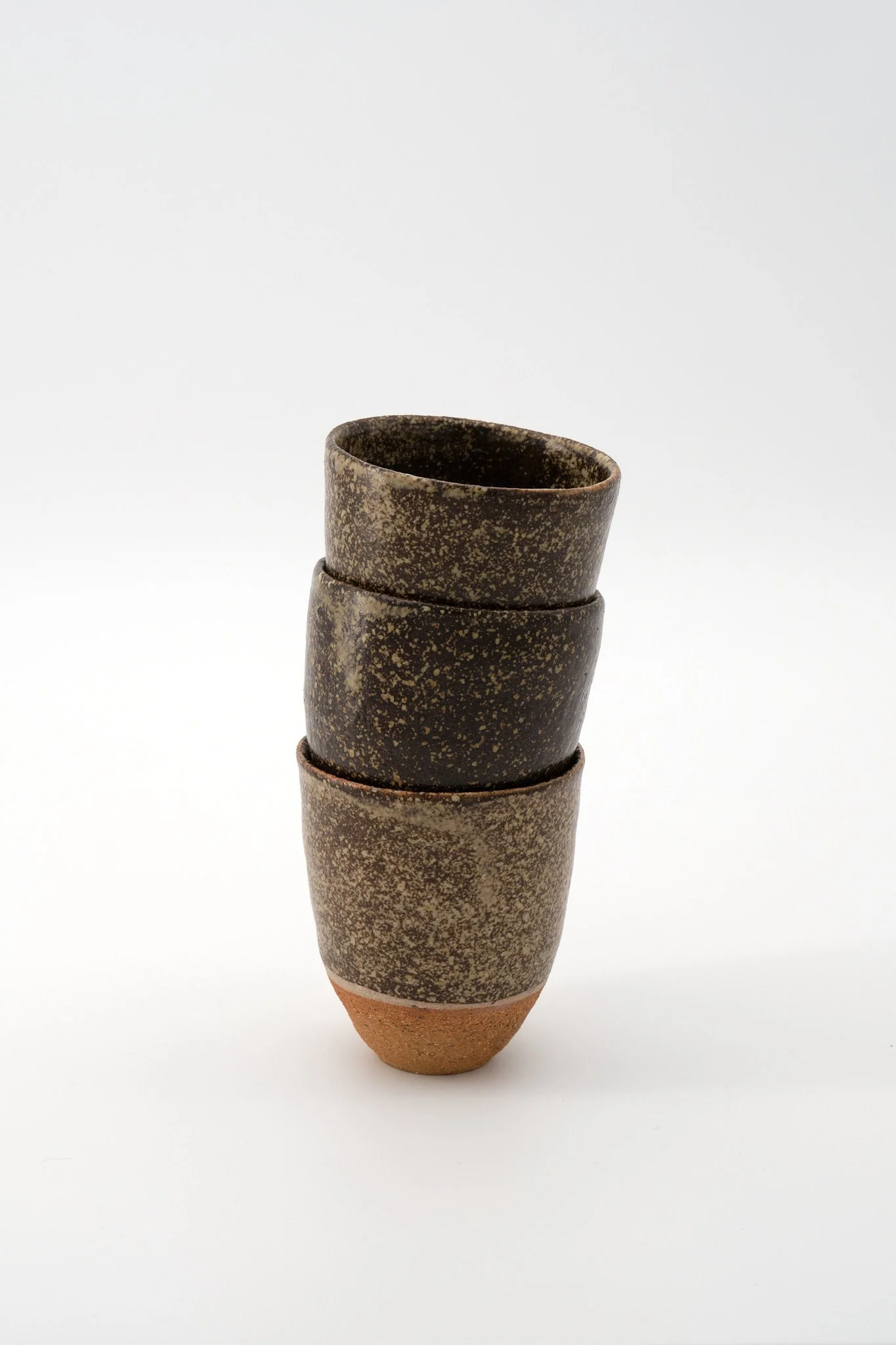 A stack of four rustic, speckled brown and black ceramic vases with a tapered reddish-brown base, arranged vertically against a plain white background.