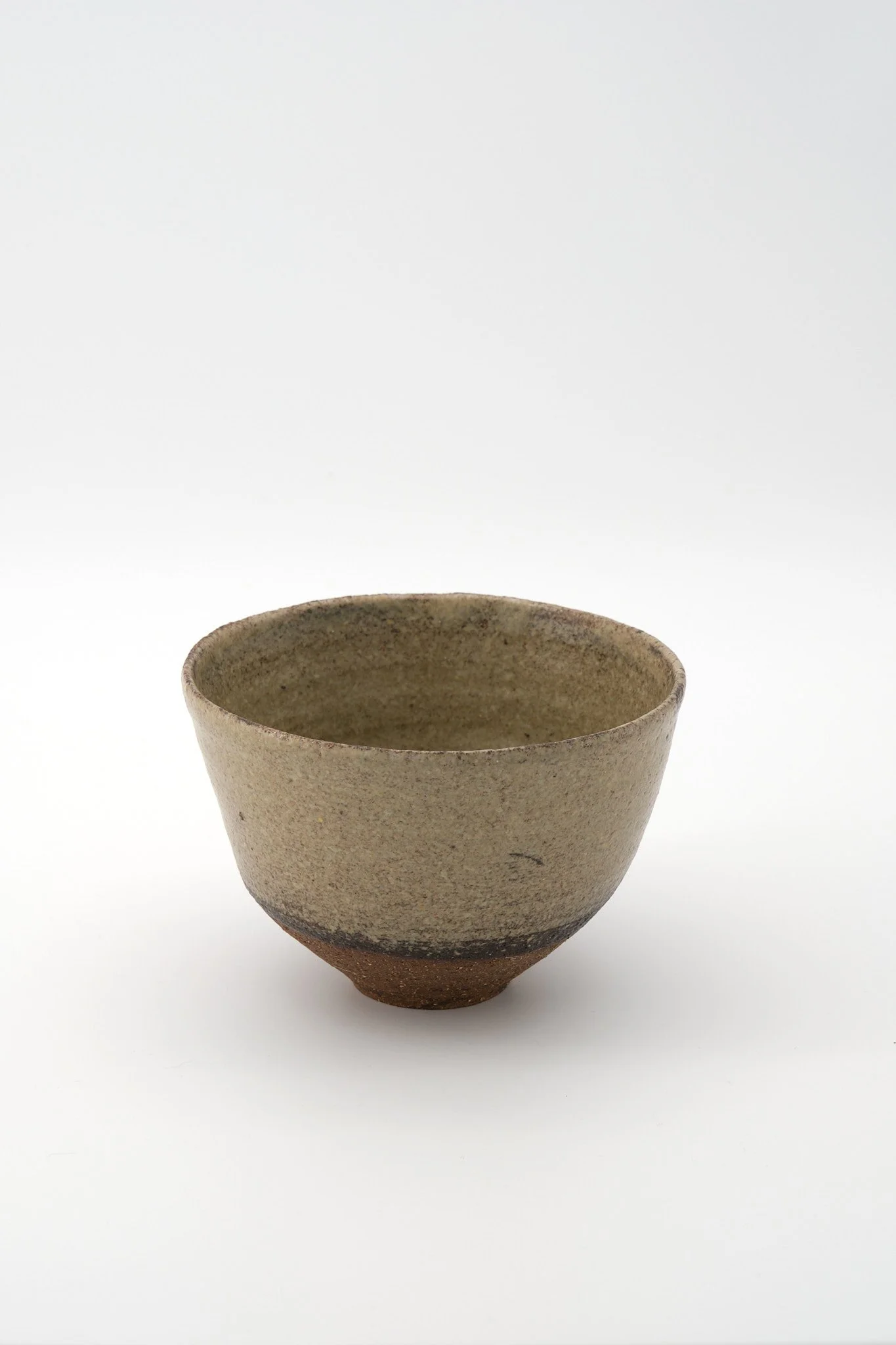A simple, rustic beige ceramic cup with a slightly textured surface, set against a plain white background.