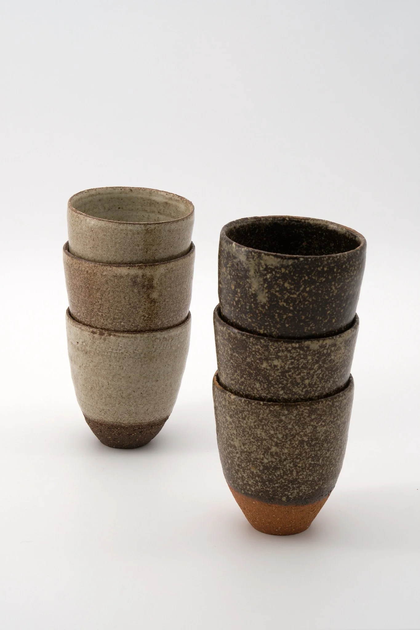 A collection of eight stacked ceramic cups with varying earthy tones and textures, arranged in two columns against a plain white background.