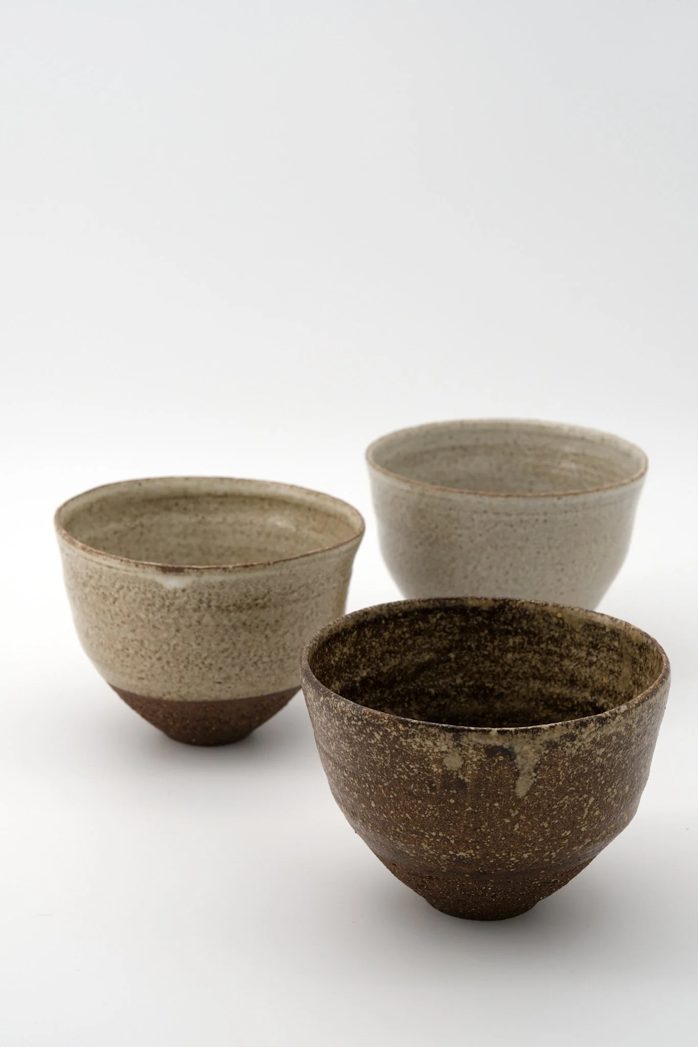 Four ceramic bowls with earthy tones, arranged on a white background, with the front bowl having a darker, speckled exterior.