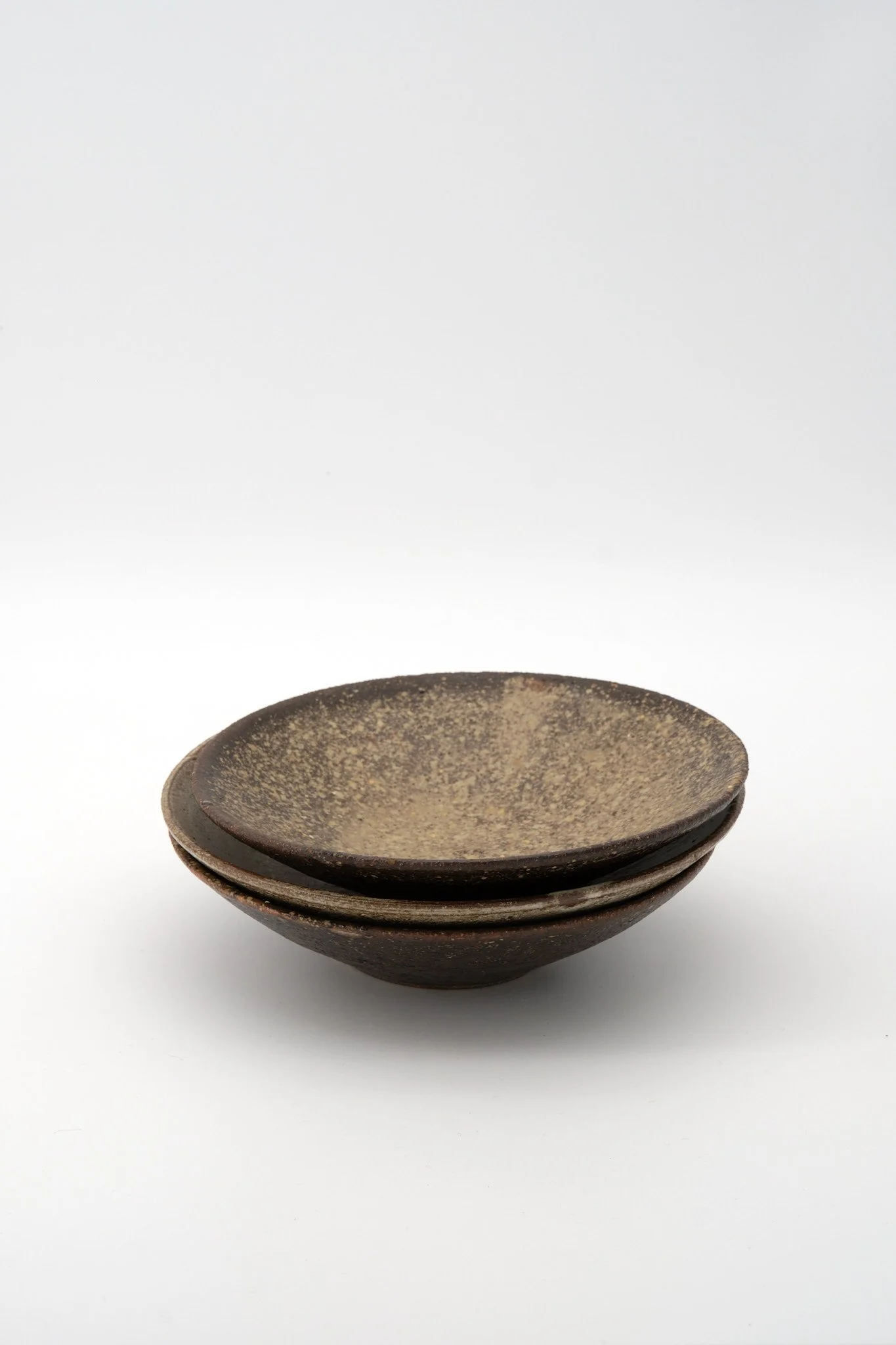 A set of three stacked dark brown ceramic bowls with a rustic, textured finish, placed against a plain white background.