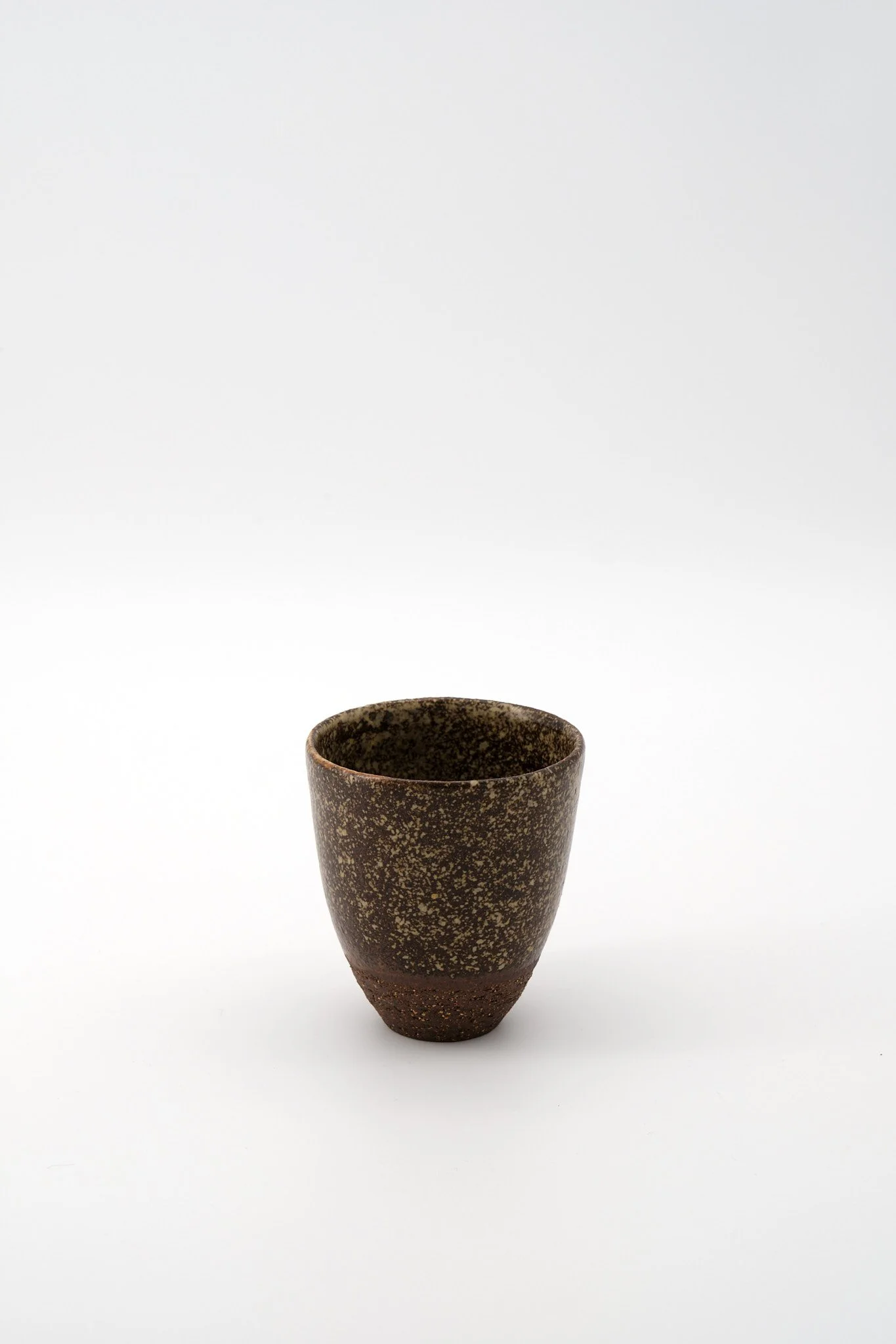 A dark brown ceramic cup with a speckled pattern, tapering at the bottom, set against a plain white background.