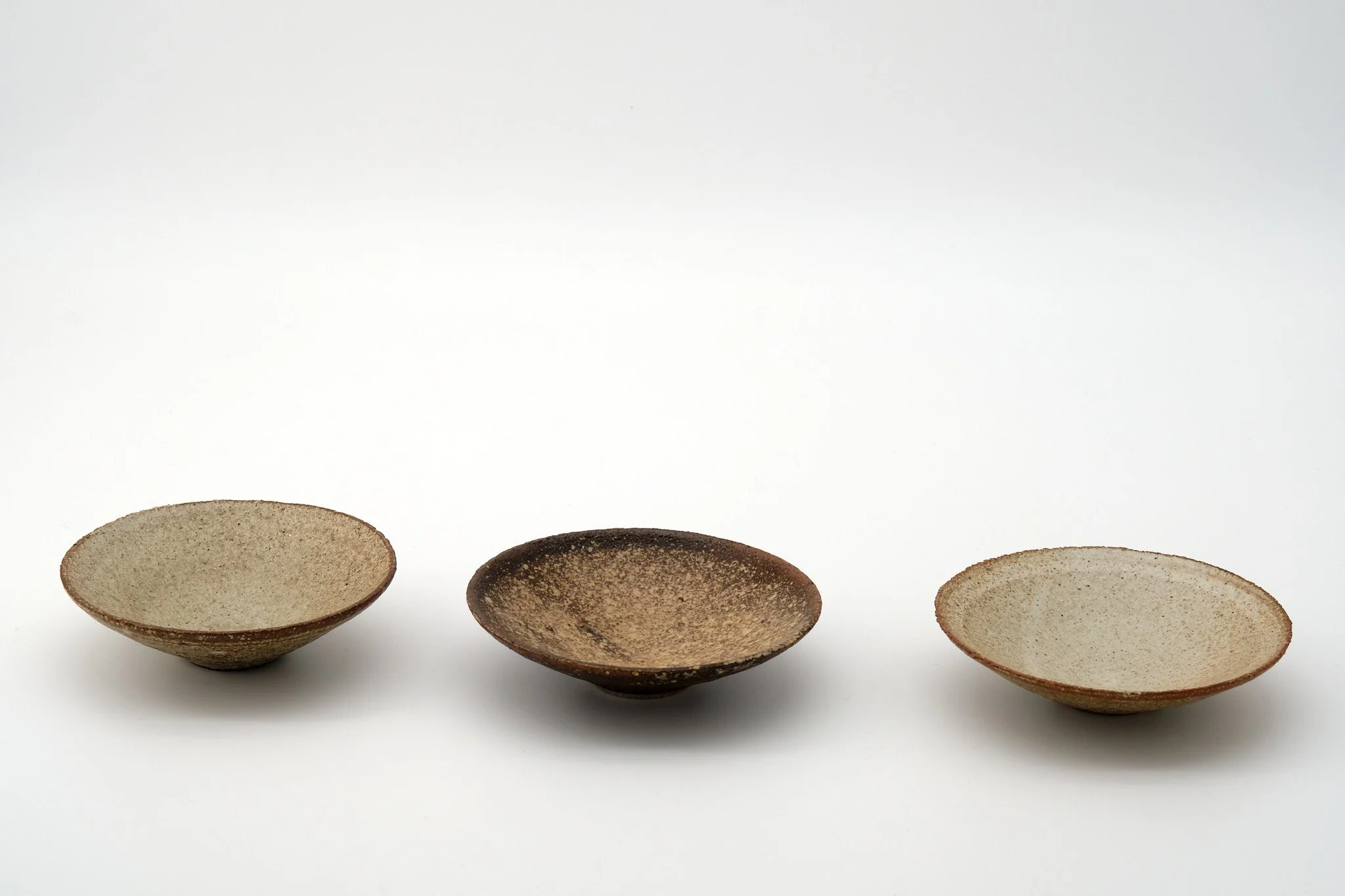 Four small ceramic bowls with earthy tones lined up on a white background.