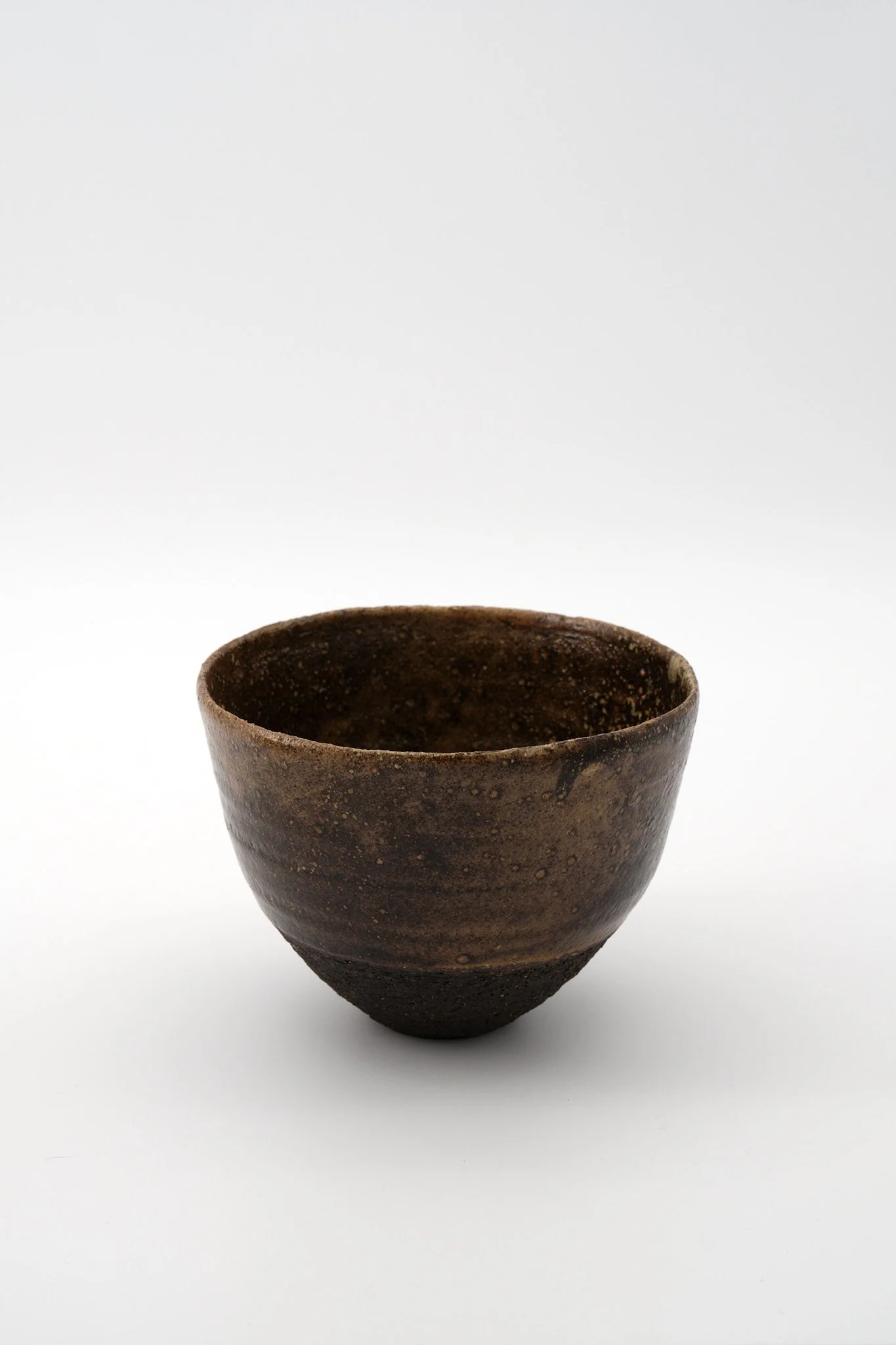 A dark brown, textured ceramic cup with a rough surface, placed on a white background.