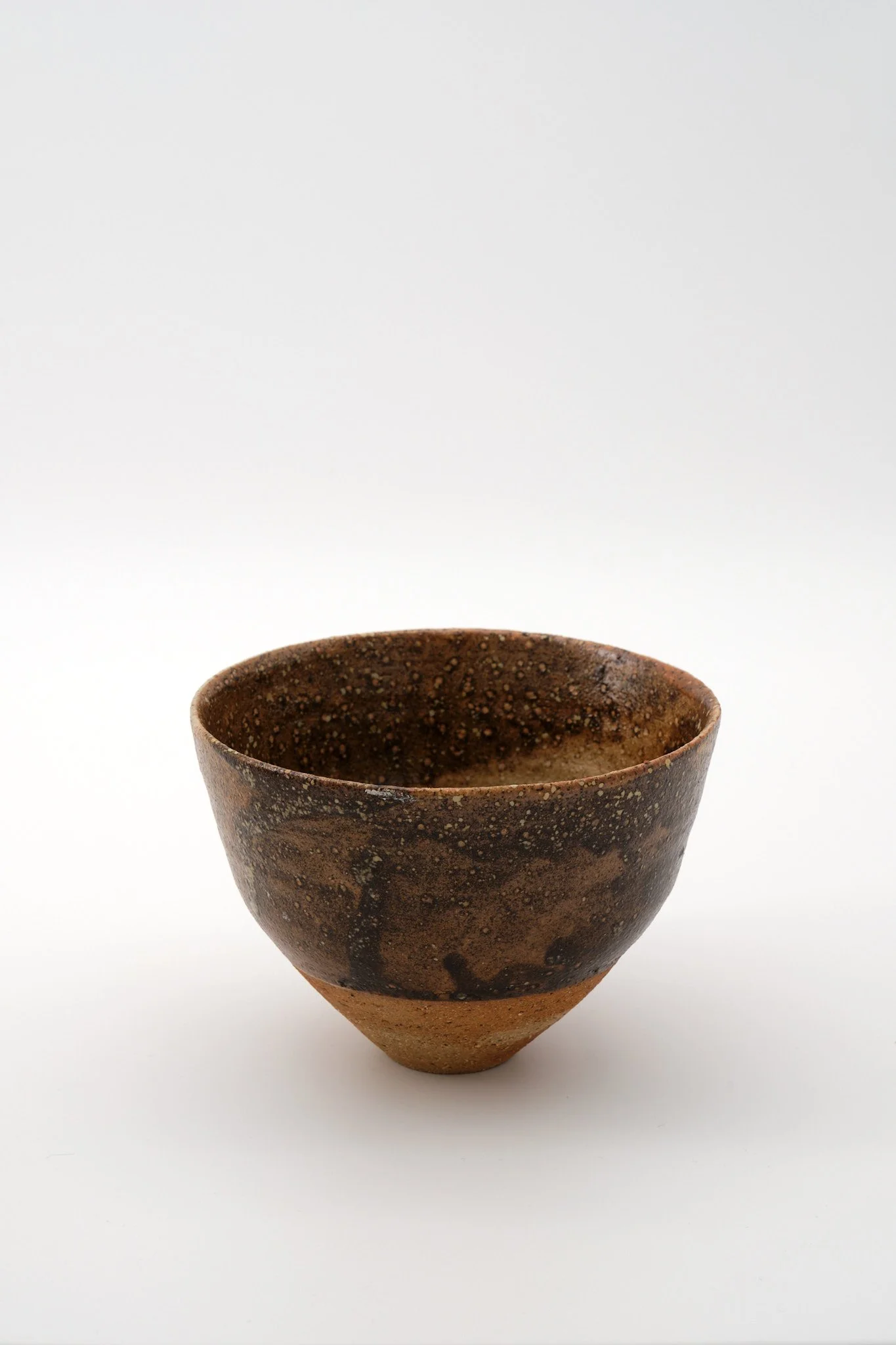 A rustic, handmade ceramic bowl with a speckled brown and black glaze, set against a white background.